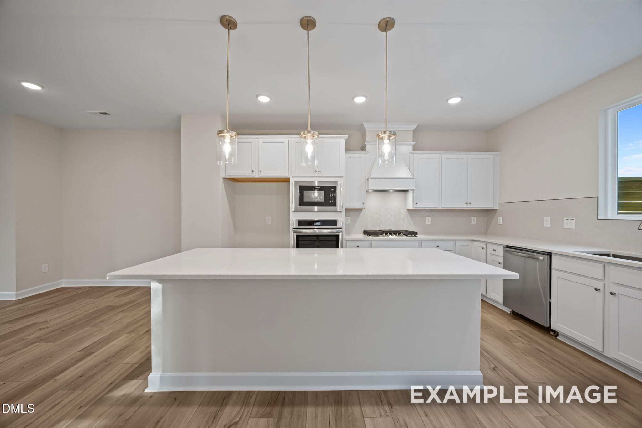 Bright modern kitchen with white shaker cabinets, quartz island, stainless appliances, gold pendants in Davidson Homes Avery, Knightdale NC