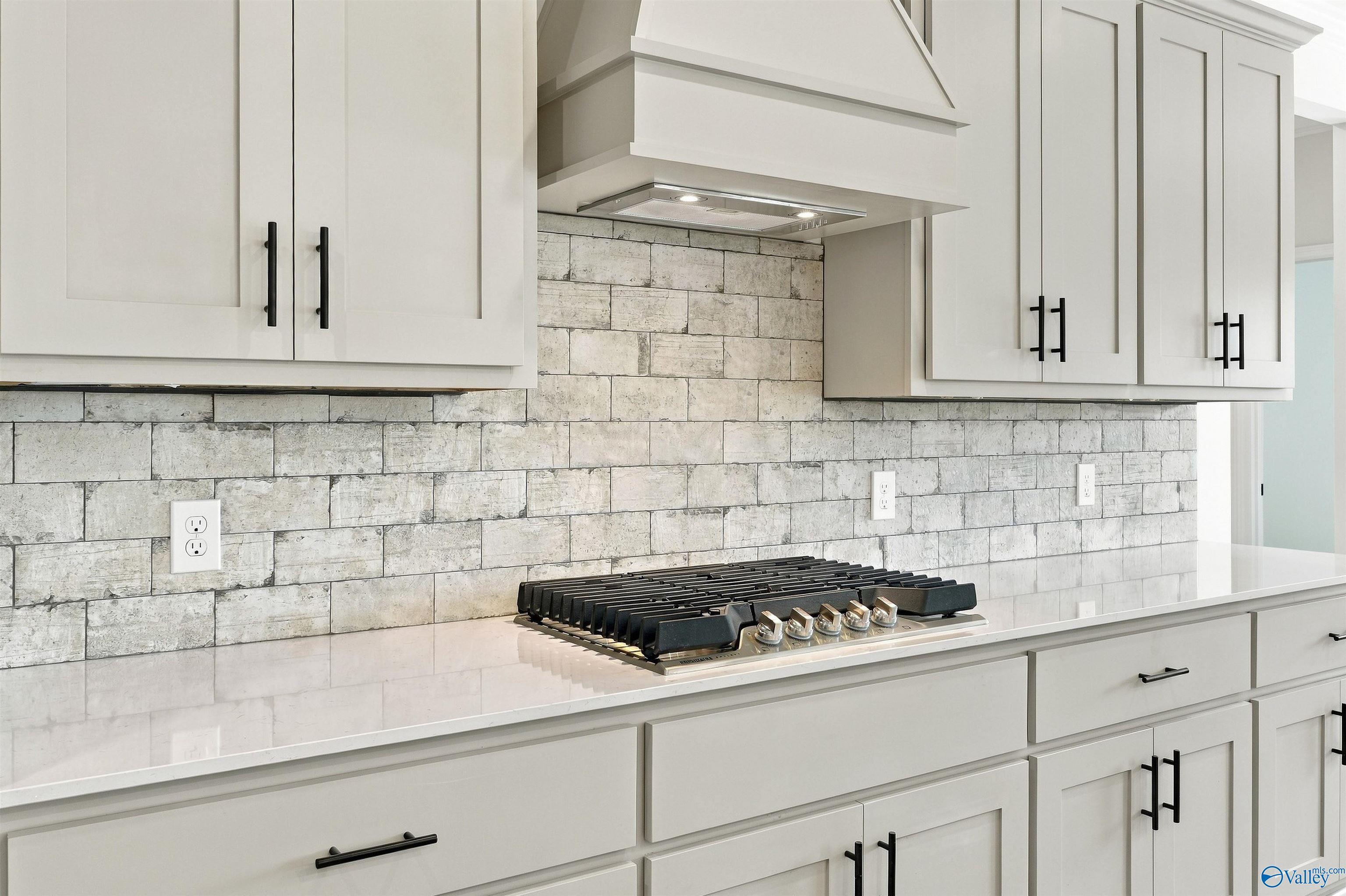 Gas cooktop with white shiplap backsplash, custom hood, and black hardware in Davidson Homes Valencia kitchen, Huntsville, Alabama