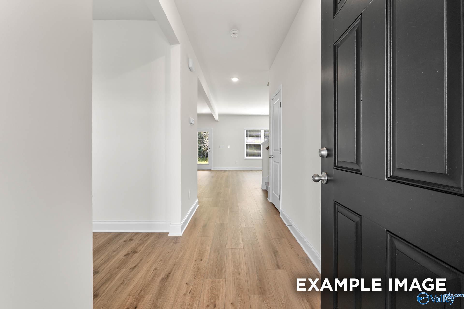 Spacious hallway with hardwood floors, white walls, and open doors in Davidson Homes The Shelby A, Hazel Green, Alabama