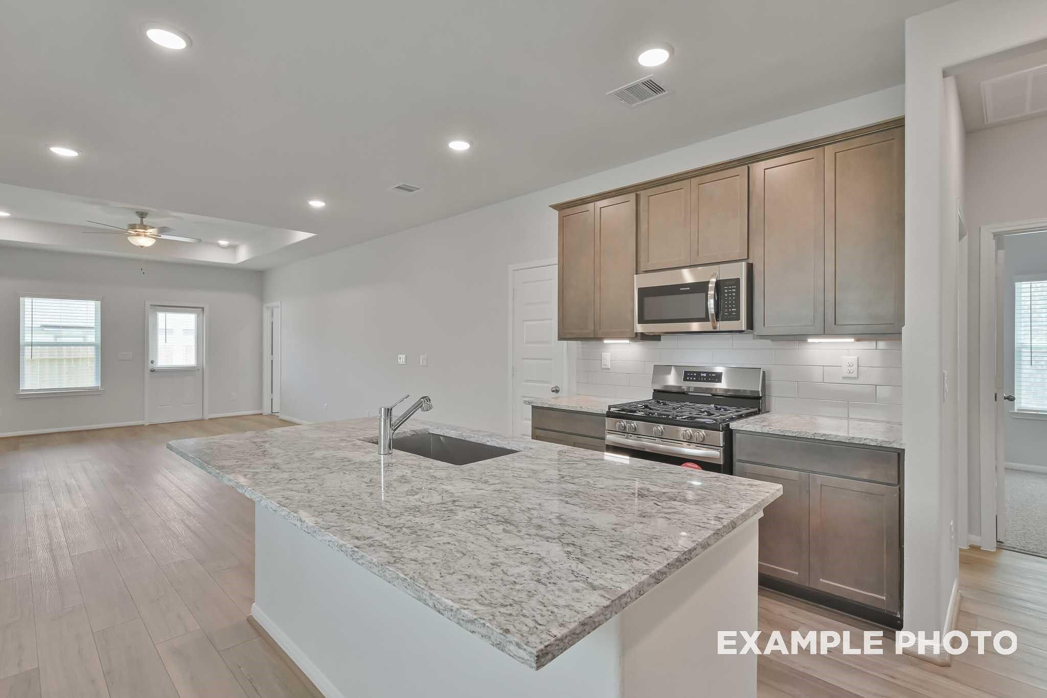 Modern open-concept kitchen with granite island, stainless steel appliances, and shaker cabinets in Davidson Homes The Frio F, Conroe, Texas