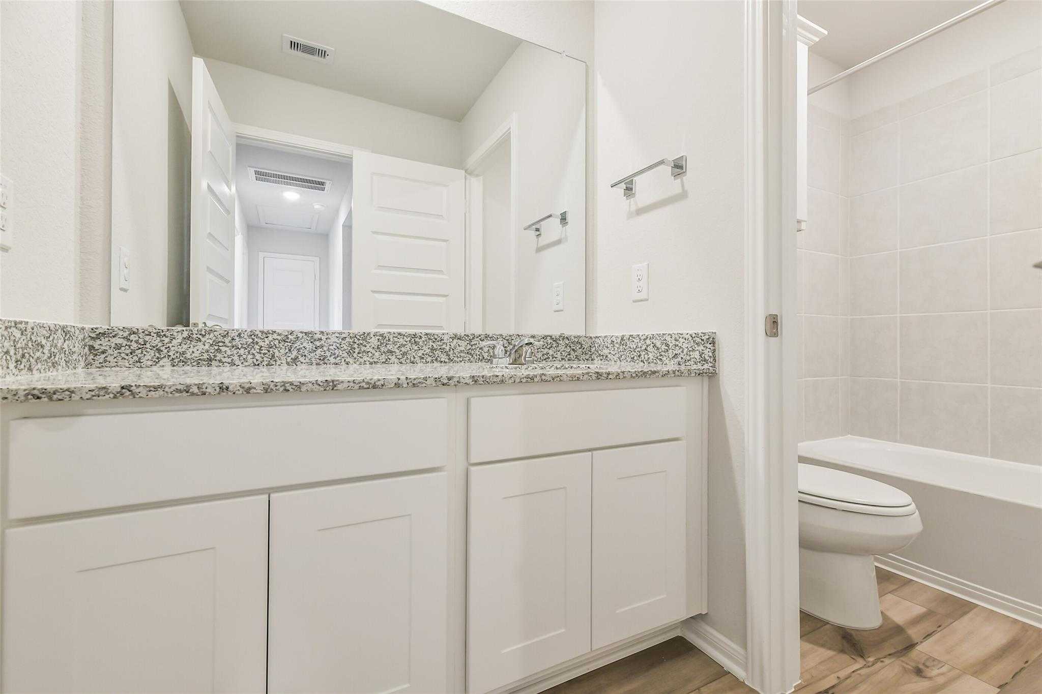Modern bathroom featuring double white vanity, granite countertop, large mirror, subway tile walls in The Brazos F by Davidson Homes, Conroe, TX