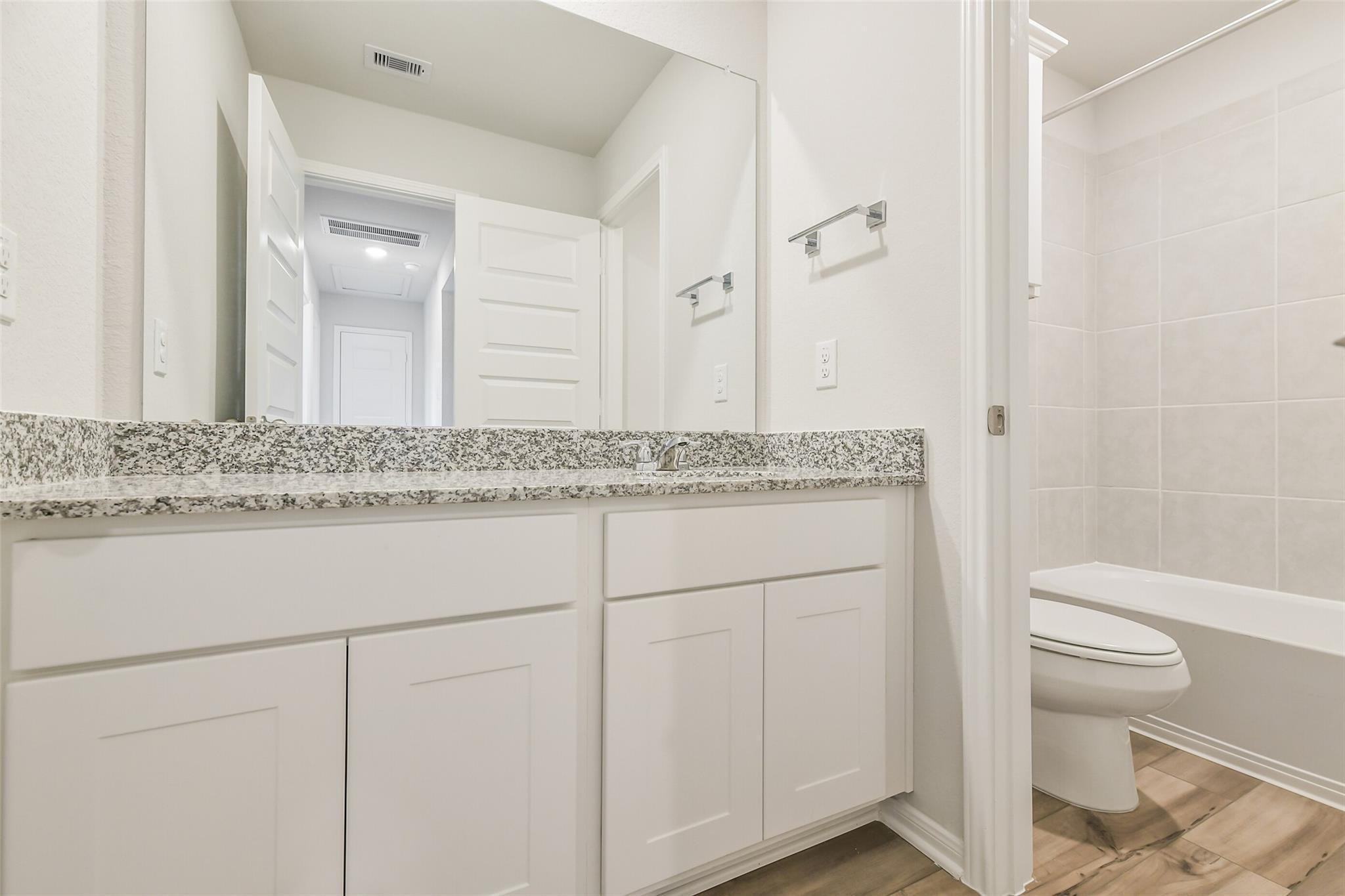 Modern bathroom with granite vanity, white shaker cabinets, subway tile walls, and hardwood floors in Davidson Homes The Brazos F, Conroe, Texas