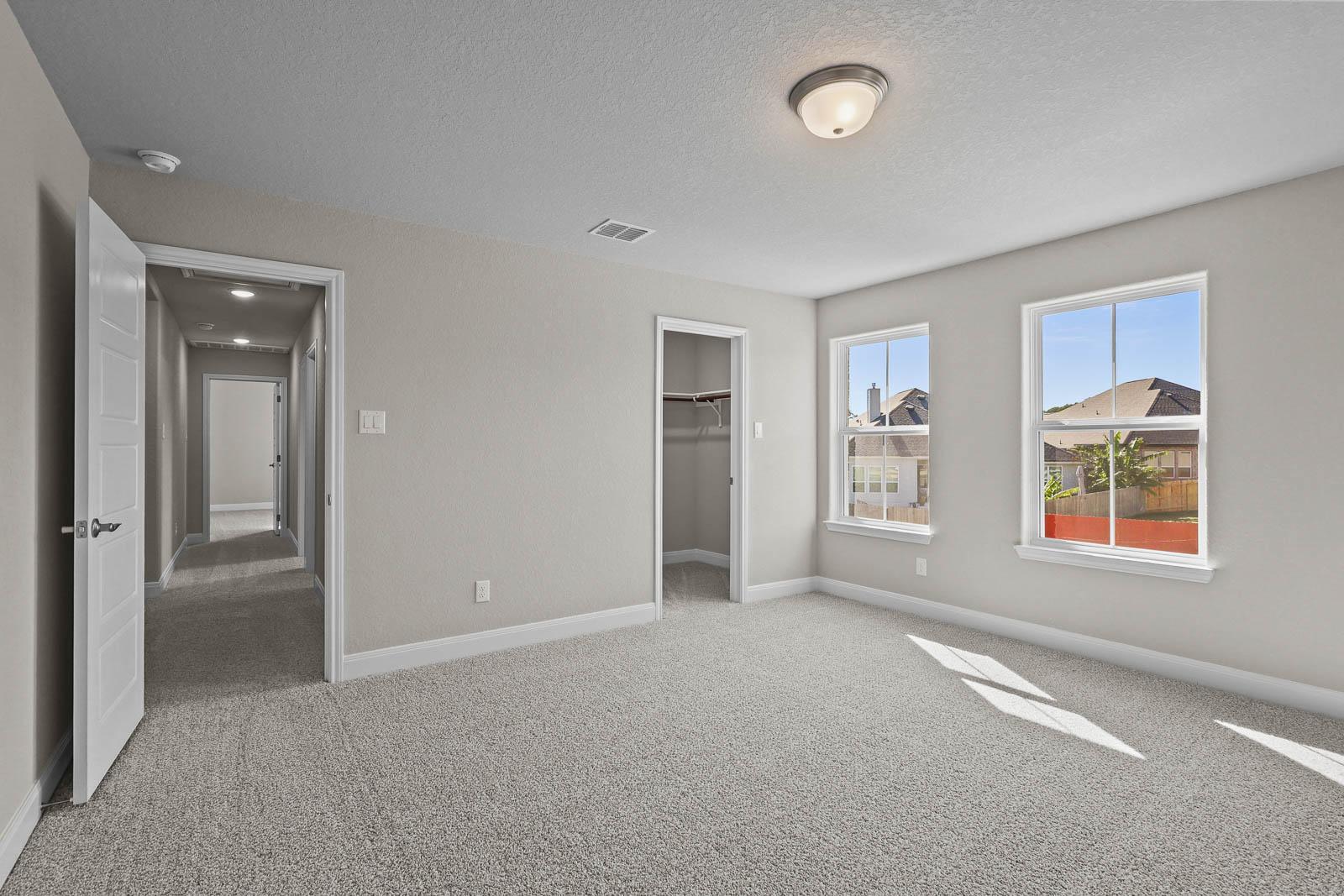 Spacious bedroom in The Jennings G featuring plush carpeting, walk-in closet, and natural light in Castroville, Texas.