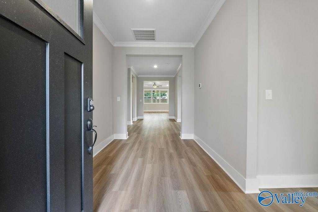 Open entryway with black door revealing long hallway, luxury vinyl plank floors, neutral walls, and natural light in Evermore Homes The Oxford, Owens Cross Roads
