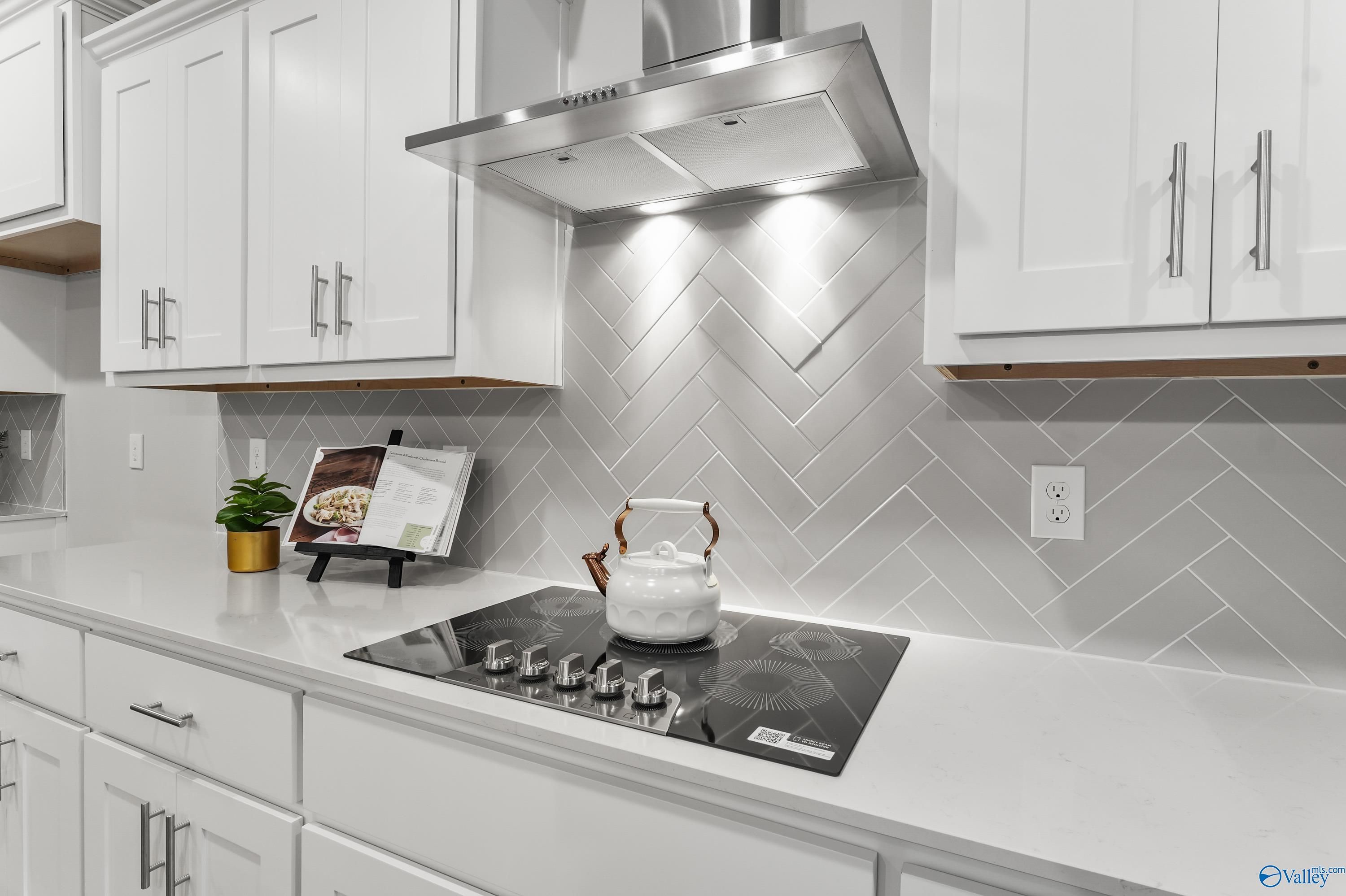 Modern kitchen featuring white shaker cabinets, gray herringbone tile backsplash, stainless range hood, and gas cooktop in The Finleigh by Davidson Homes, Toney, AL