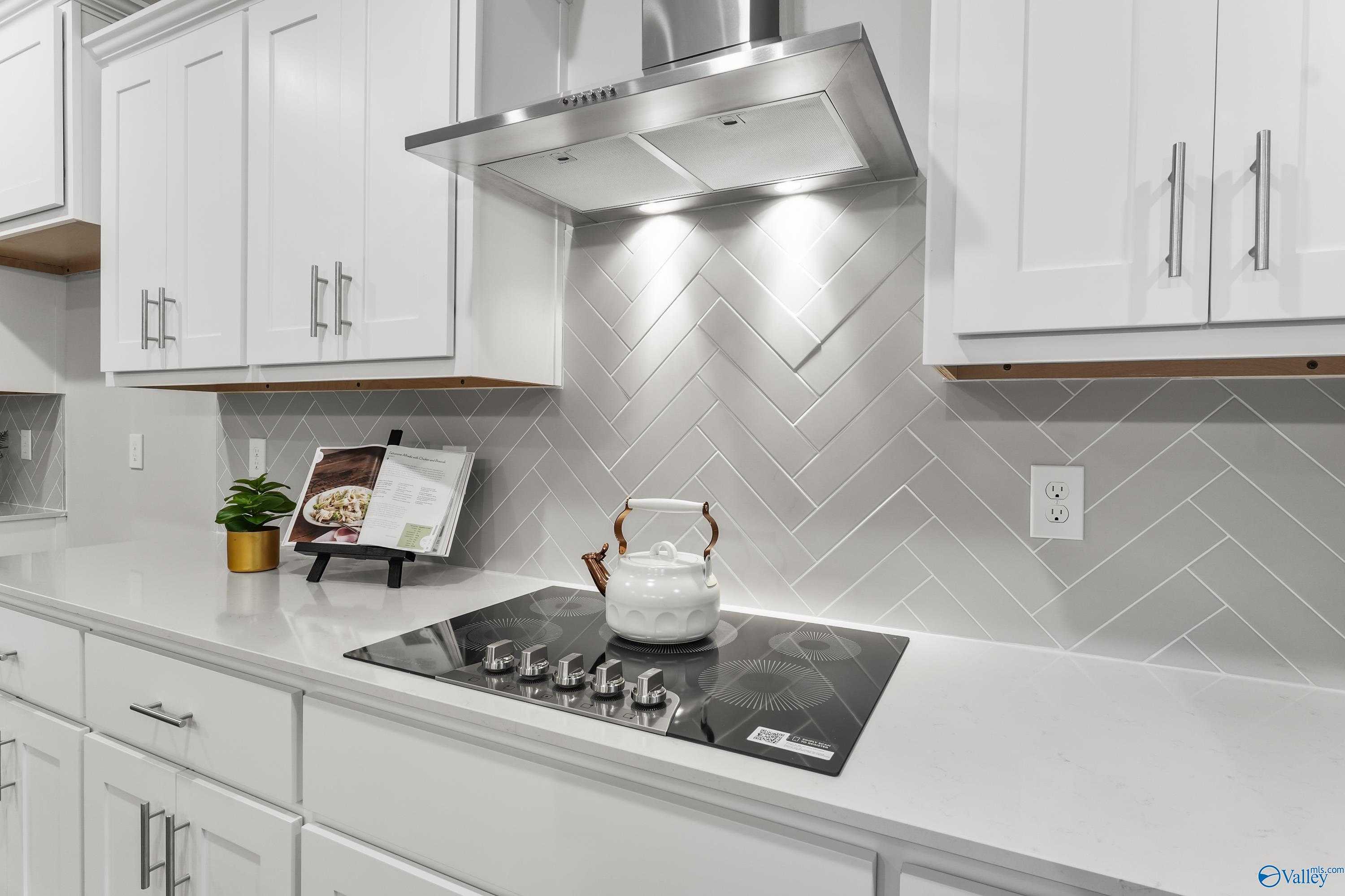 Modern kitchen featuring white shaker cabinets, gray herringbone tile backsplash, stainless range hood, and gas cooktop in The Finleigh by Davidson Homes, Toney, AL