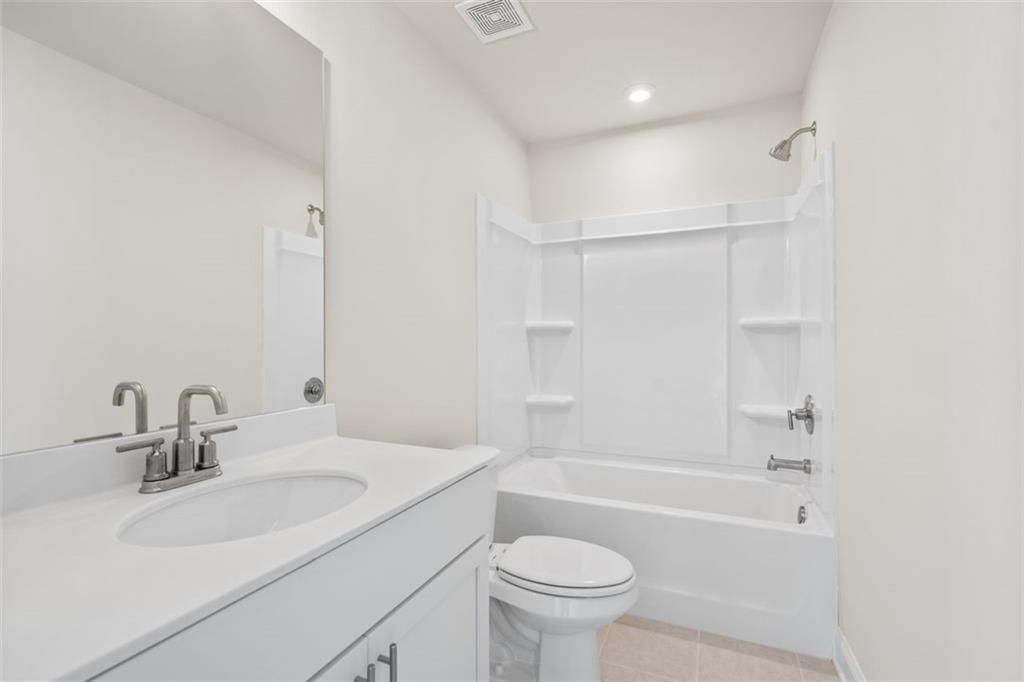 Modern white bathroom with tub-shower combo, single vanity sink, mirror, and toilet in Davidson Homes The Ash C at Wehunt Meadows, Hoschton