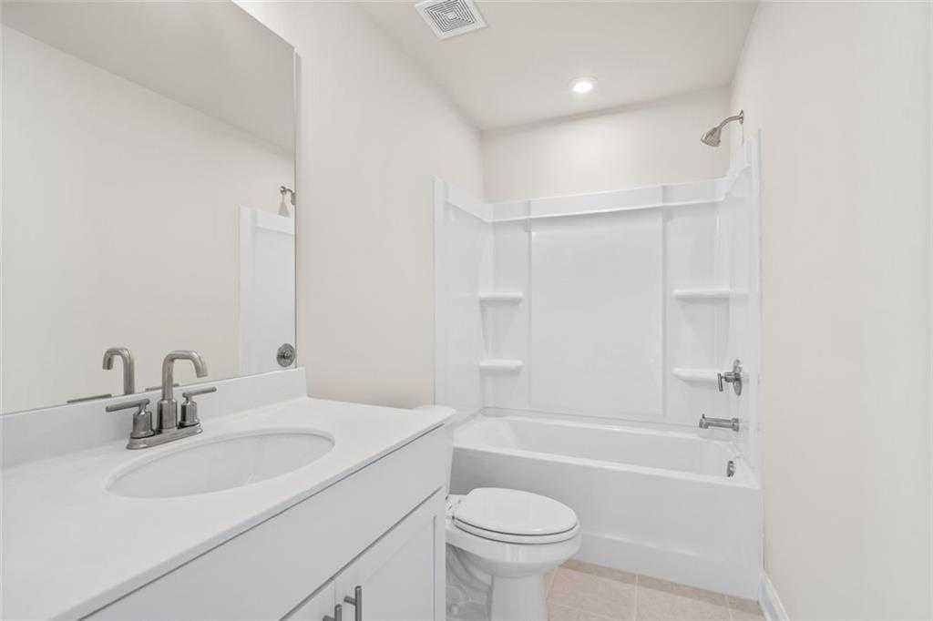 Modern white bathroom with tub-shower combo, single vanity sink, mirror, and toilet in Davidson Homes The Ash C at Wehunt Meadows, Hoschton