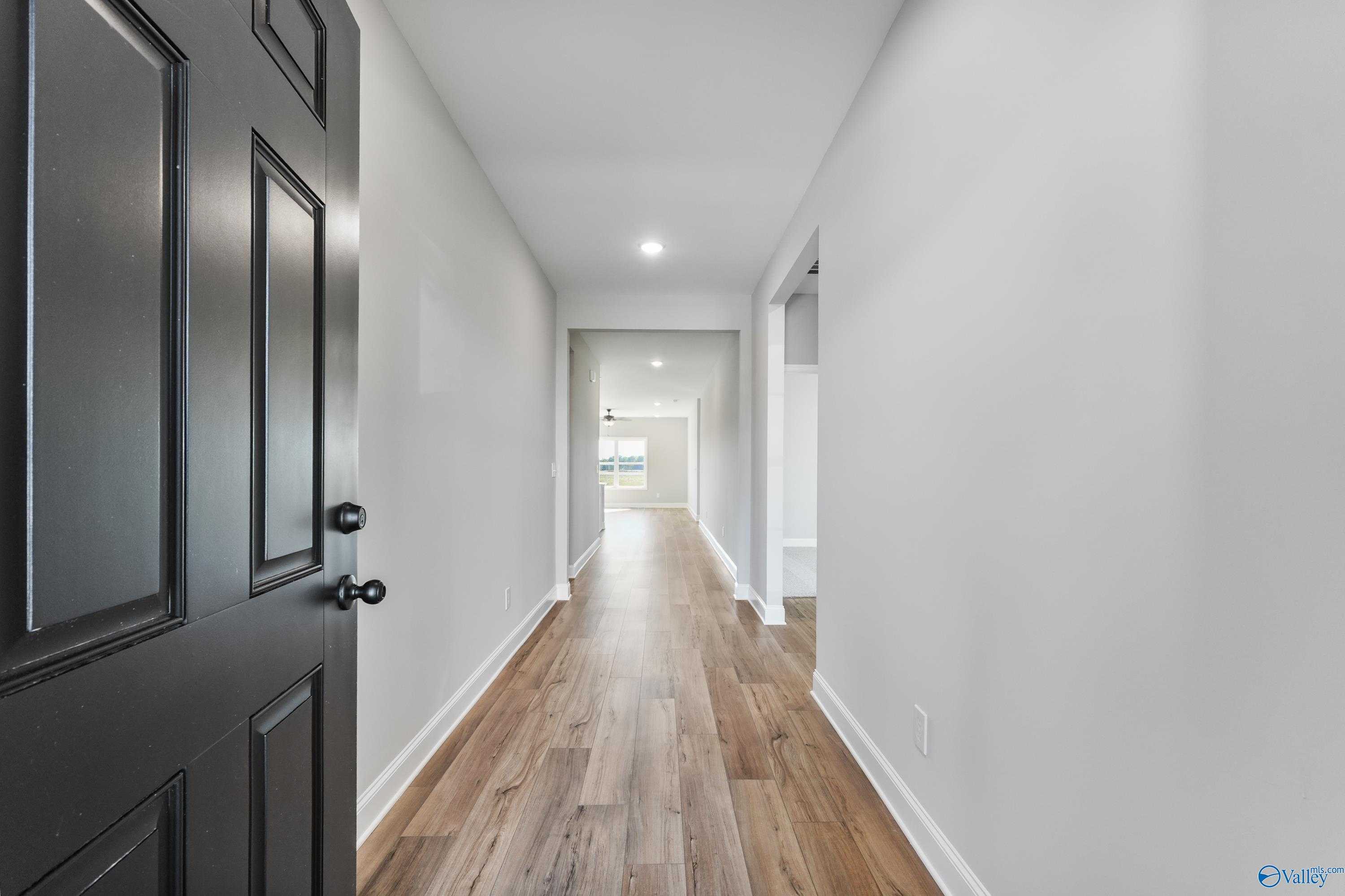 Spacious entry hallway with open black door, hardwood floors, and white walls in Davidson Homes The Daphne C, Hazel Green, AL
