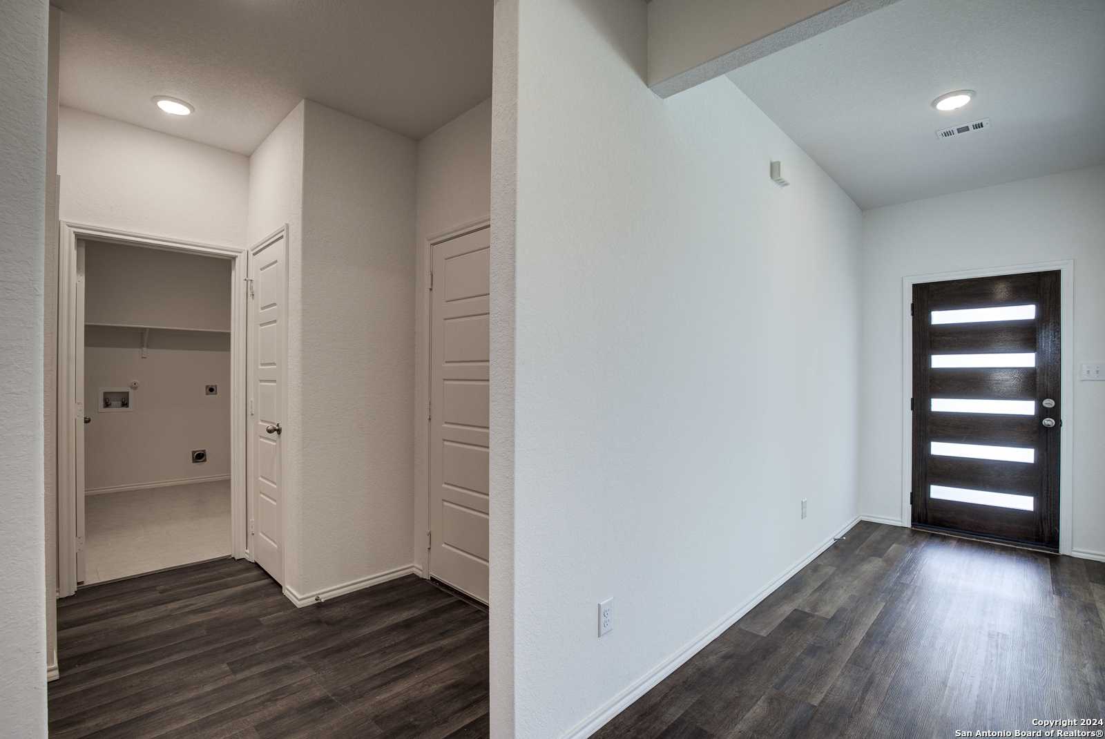 Modern laundry room with utility sink and adjacent entry foyer featuring frosted glass door in The Douglas D, Seguin, Texas