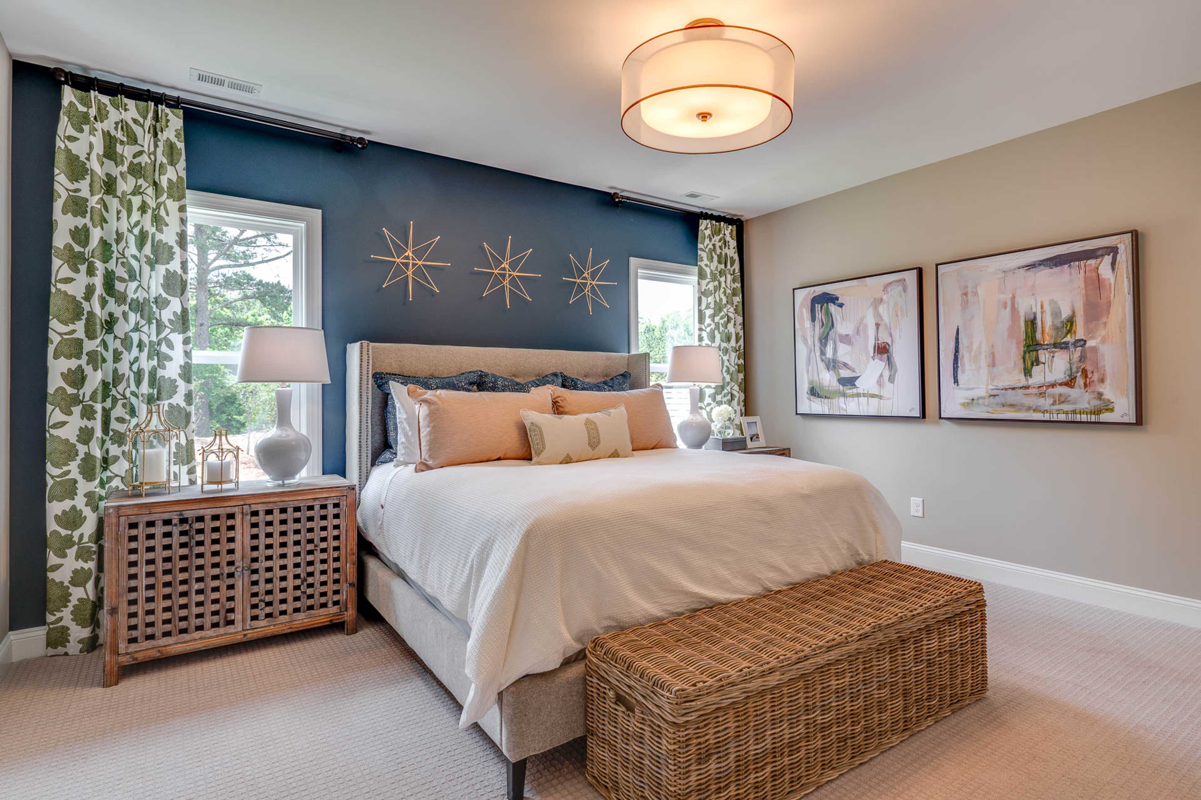 Spacious master bedroom at Hasentree in Wake Forest NC with navy accent wall, king bed, abstract art, and wicker bench