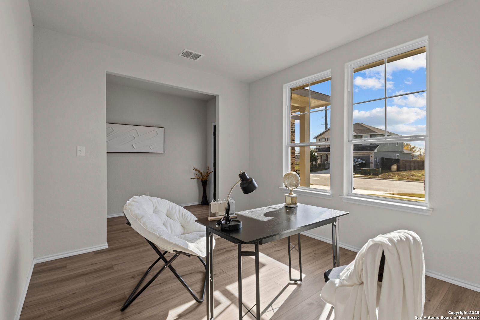 Sunny home office with wooden desk, white pouf chair, large windows in The Douglas C floor plan, Hannah Heights, Seguin Texas