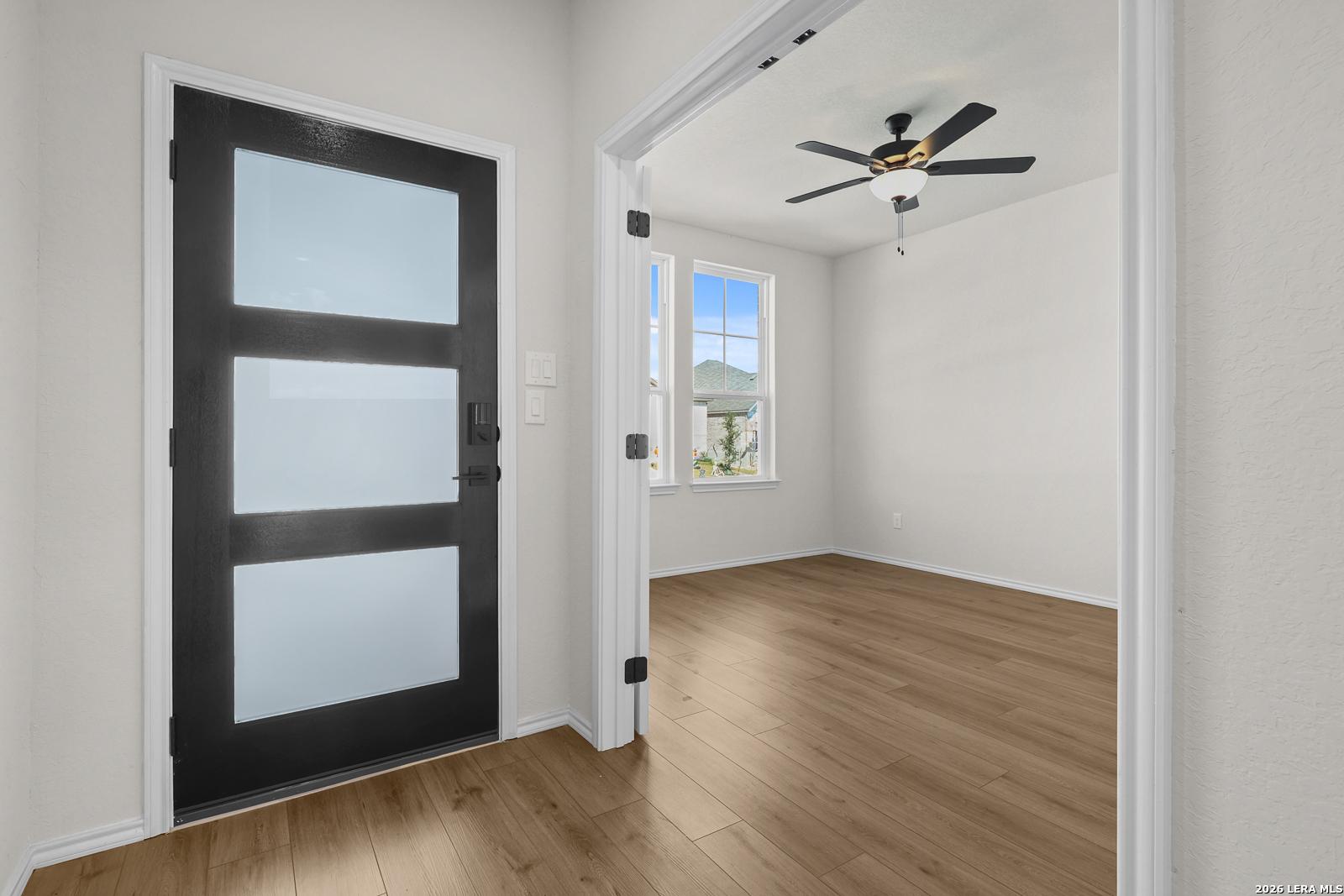 Modern black front door with frosted glass panels opening to bright living room with hardwood floors in Davidson Homes Glenwood E, San Antonio