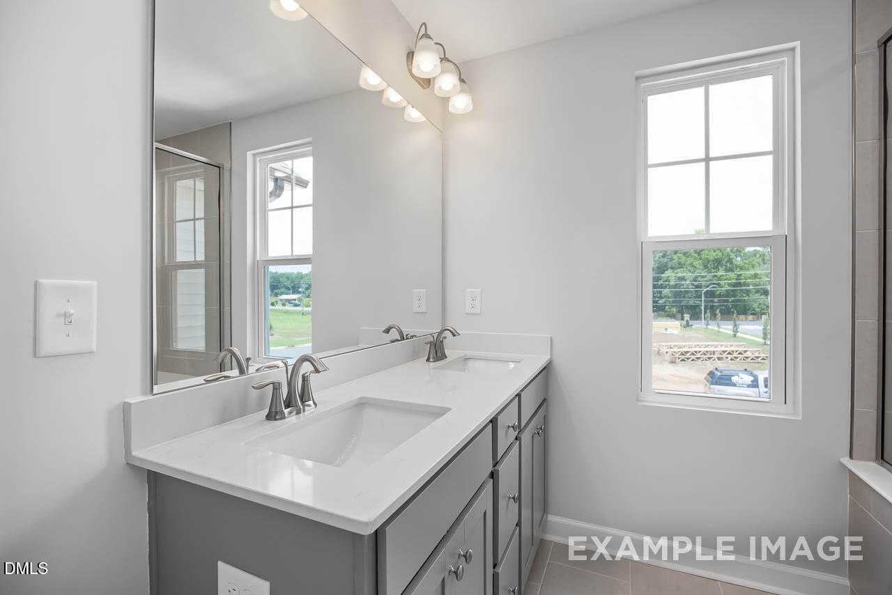 Modern double vanity bathroom with white quartz counters, gray cabinets, mirrors, and scenic field view in Davidson Homes The Warren, Fuquay-Varina, NC