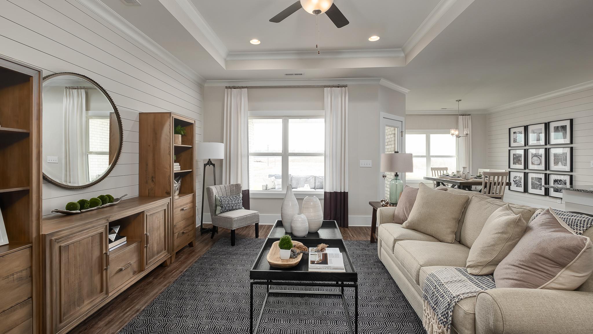 Spacious Davidson Homes living room in Raleigh with shiplap walls, wooden built-ins, beige sofa, black coffee table, and natural light
