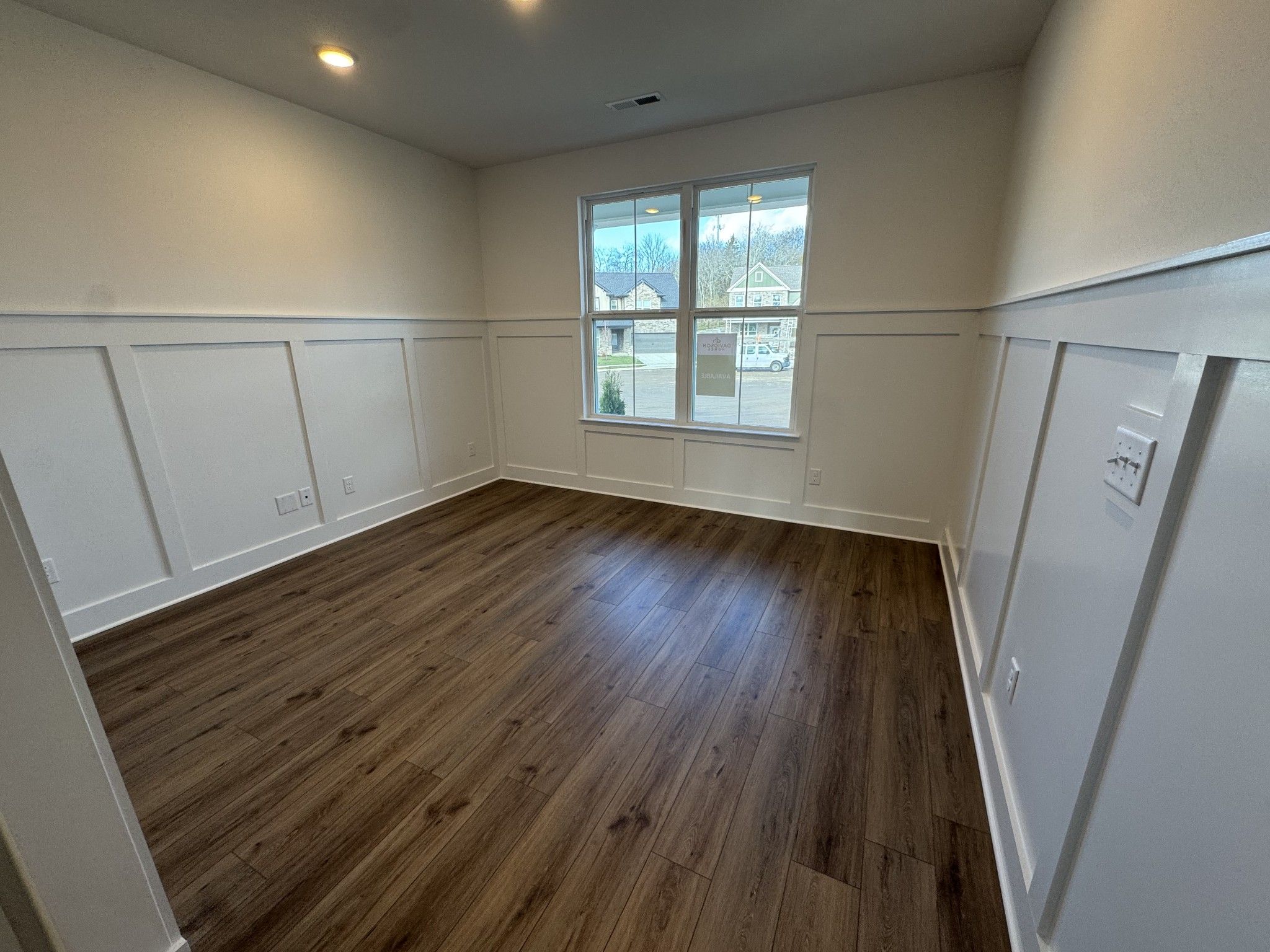 Bright secondary bedroom featuring white wainscoting, hardwood floors, and large windows in Davidson Homes The Ridgeport, Gallatin, TN