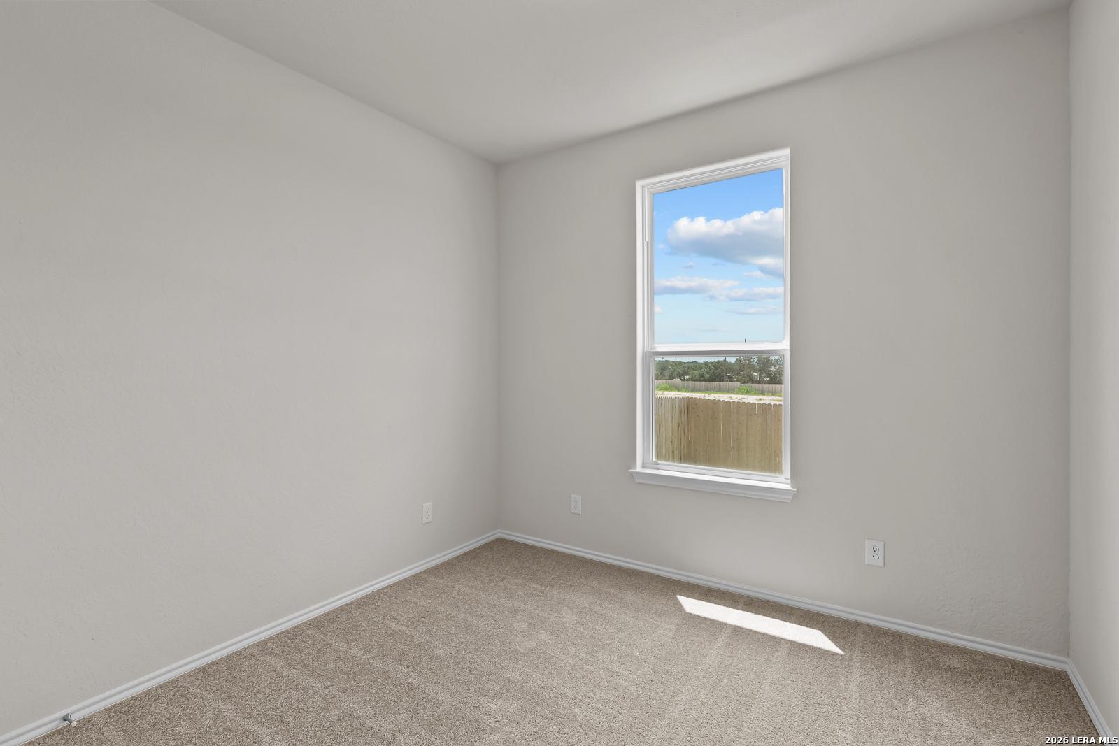 Bright, carpeted bedroom with large window in The Gillian B floor plan at Meadows at Oak Creek, San Antonio, Texas.