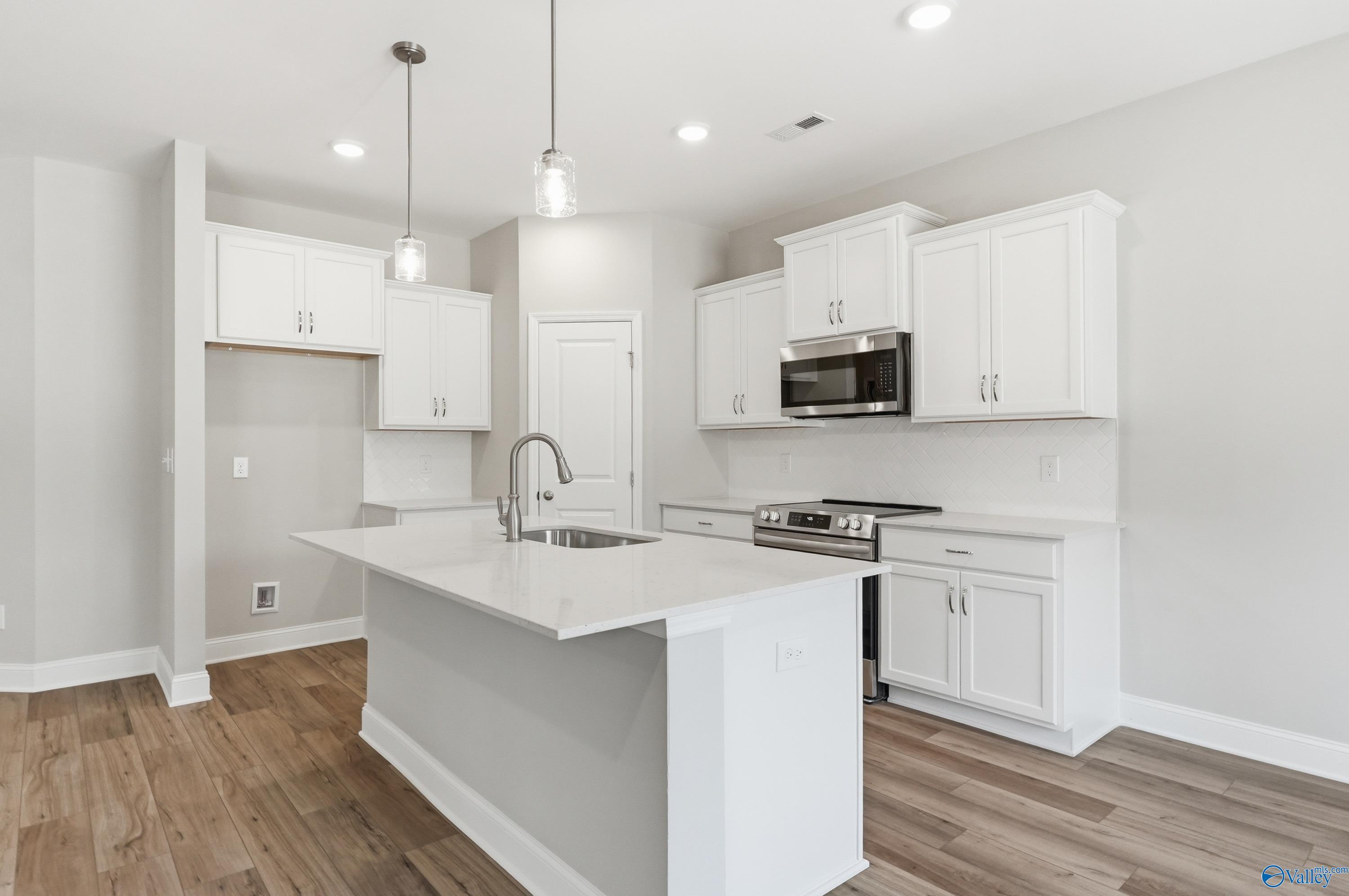 Modern white kitchen with stainless steel appliances, quartz island sink, and hardwood floors in The Asheville plan, Huntsville AL