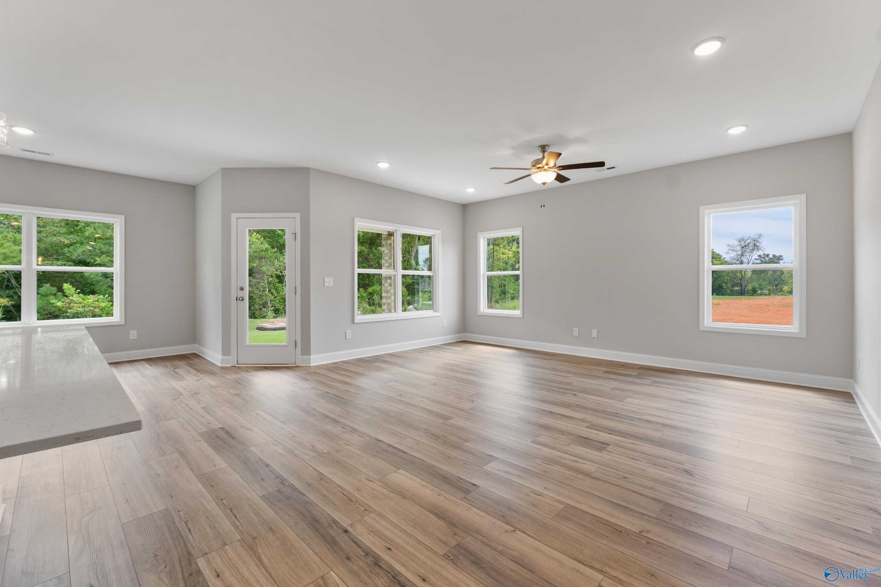 Bright open-concept living room with hardwood floors, large windows, and ceiling fan in Davidson Homes The Franklin, Huntsville, AL