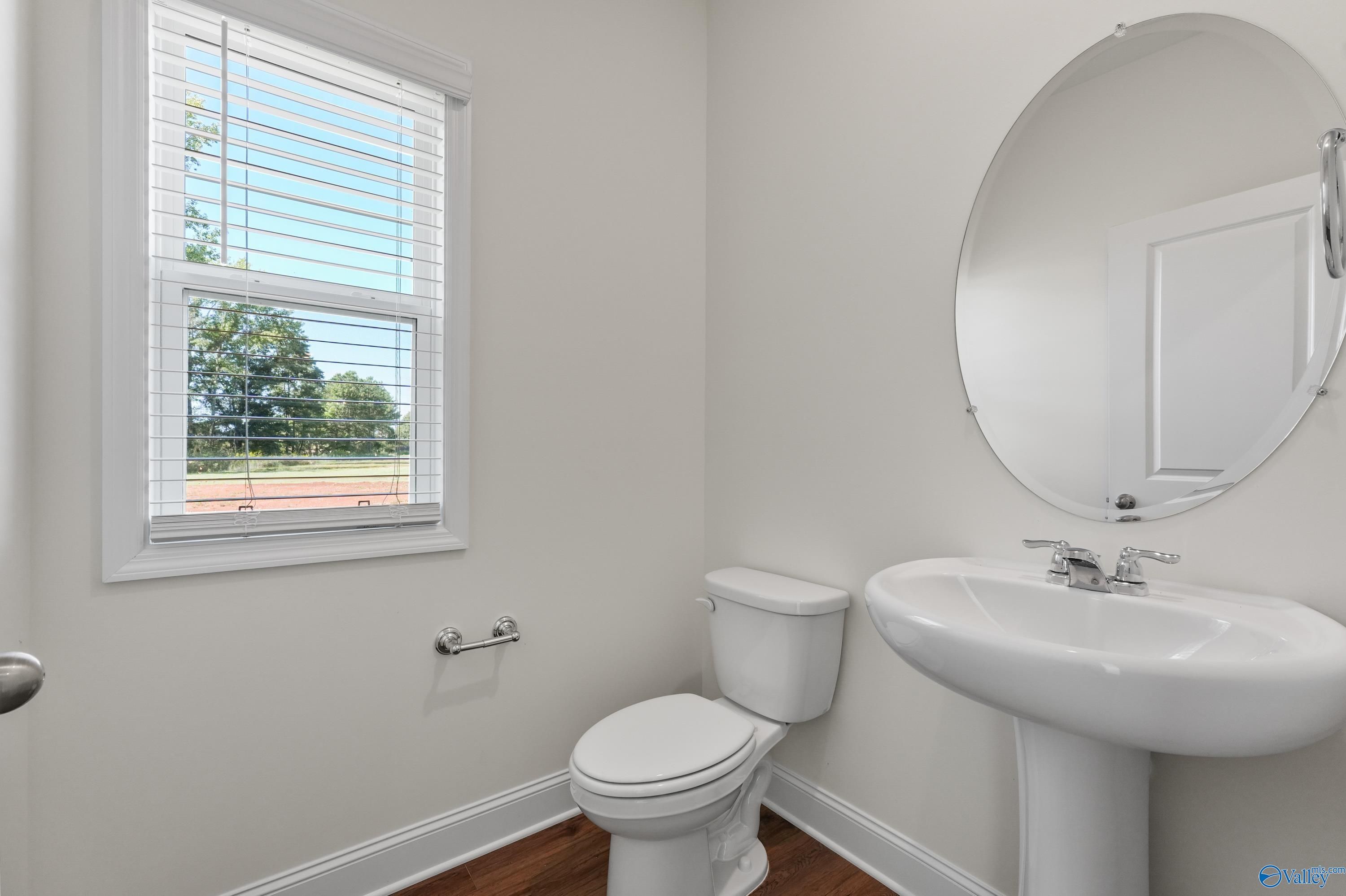 Bright powder room with pedestal sink, round mirror, and window view in Davidson Homes The Shelby A, Athens, Alabama