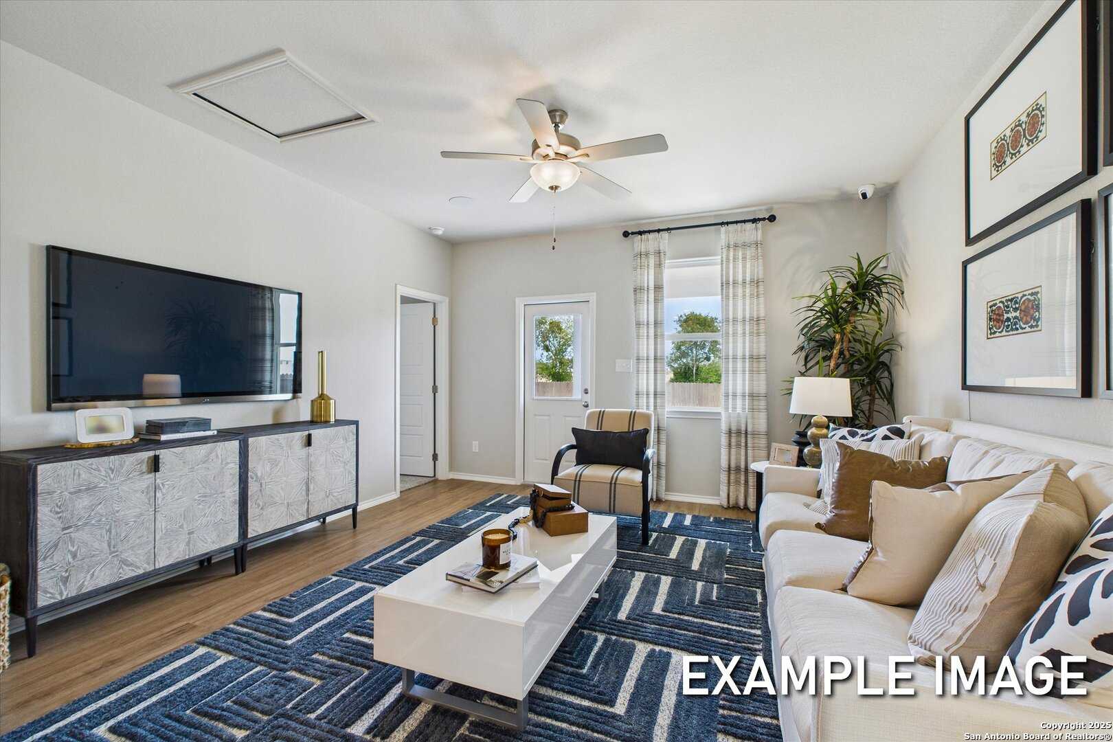 Cozy living room with wall-mounted TV, beige sofa, blue rug, and ceiling fan in Davidson Homes Sabine C, San Antonio