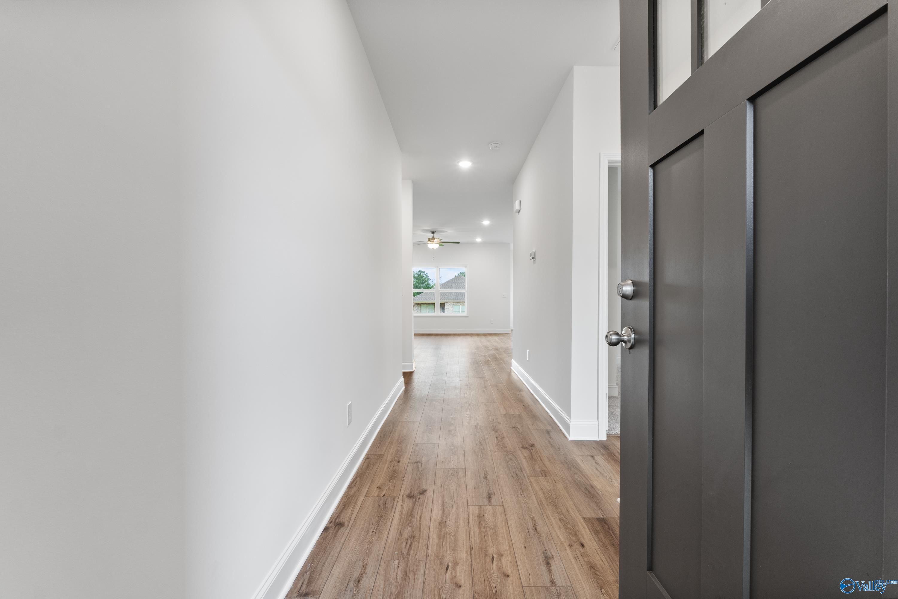 Bright hallway with luxury vinyl plank floors, white walls, and dark wood front door in Davidson Homes The Asheville C, New Market, Alabama