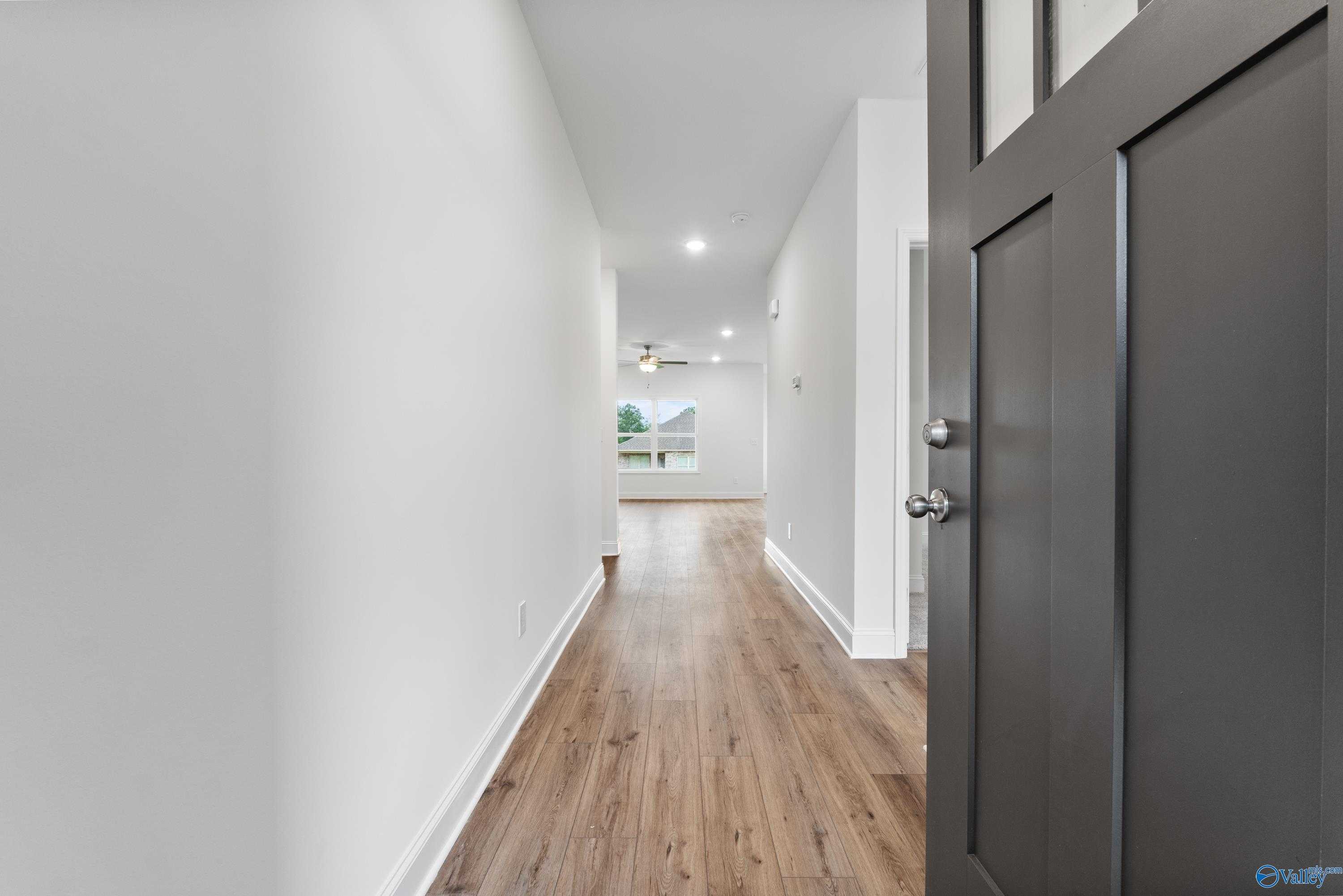 Bright hallway with luxury vinyl plank floors, white walls, and dark wood front door in Davidson Homes The Asheville C, New Market, Alabama