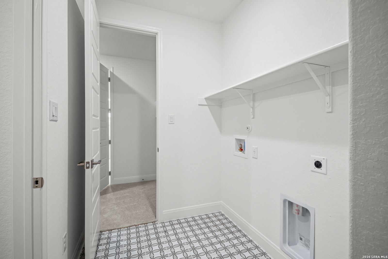 Laundry room with patterned tile flooring and shelving in The Lanier G floor plan at Potranco Oaks, Castroville, Texas.