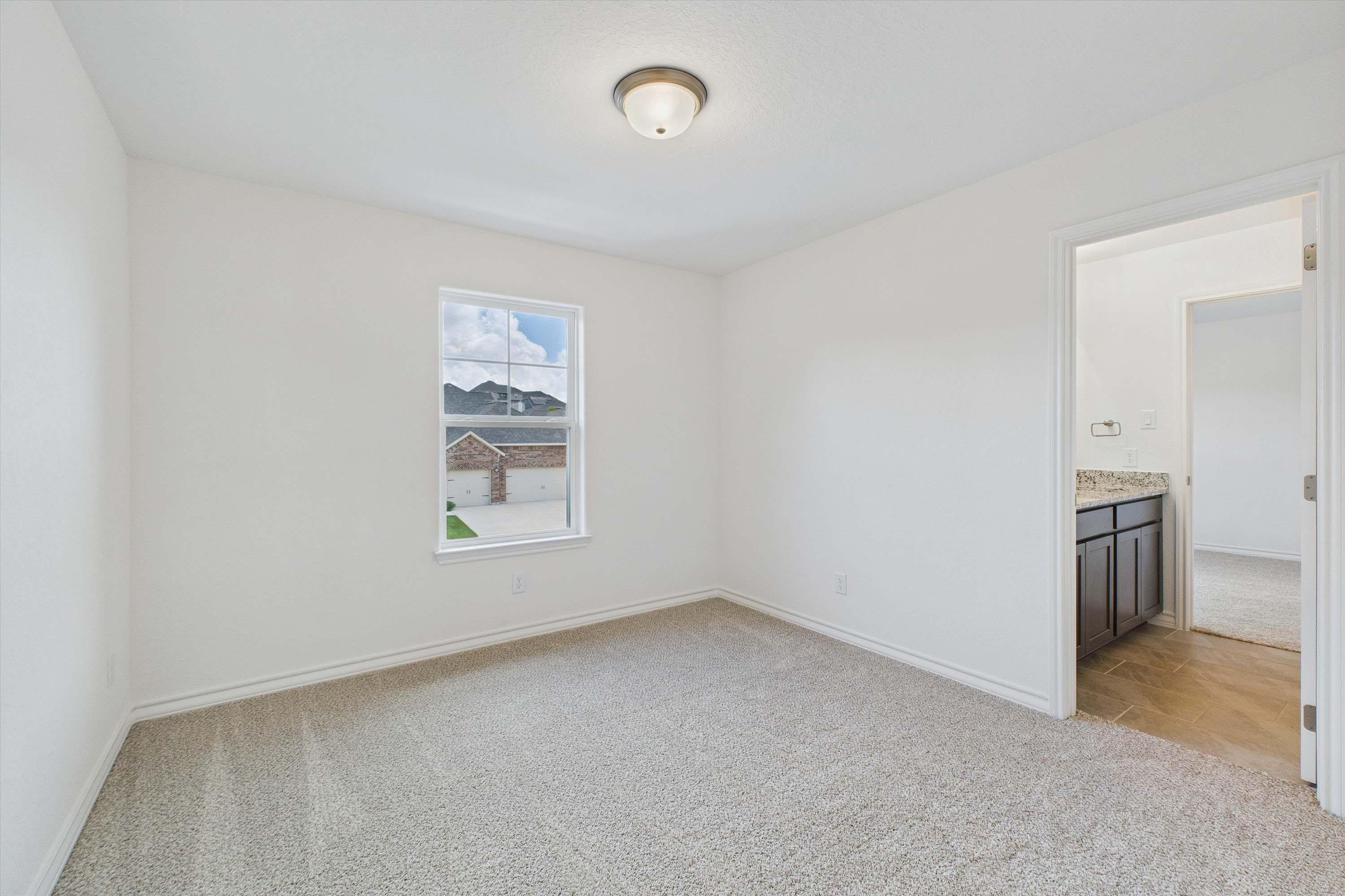 Bright secondary bedroom in The Danbury with plush carpeting, neutral walls, and an attached private bathroom.