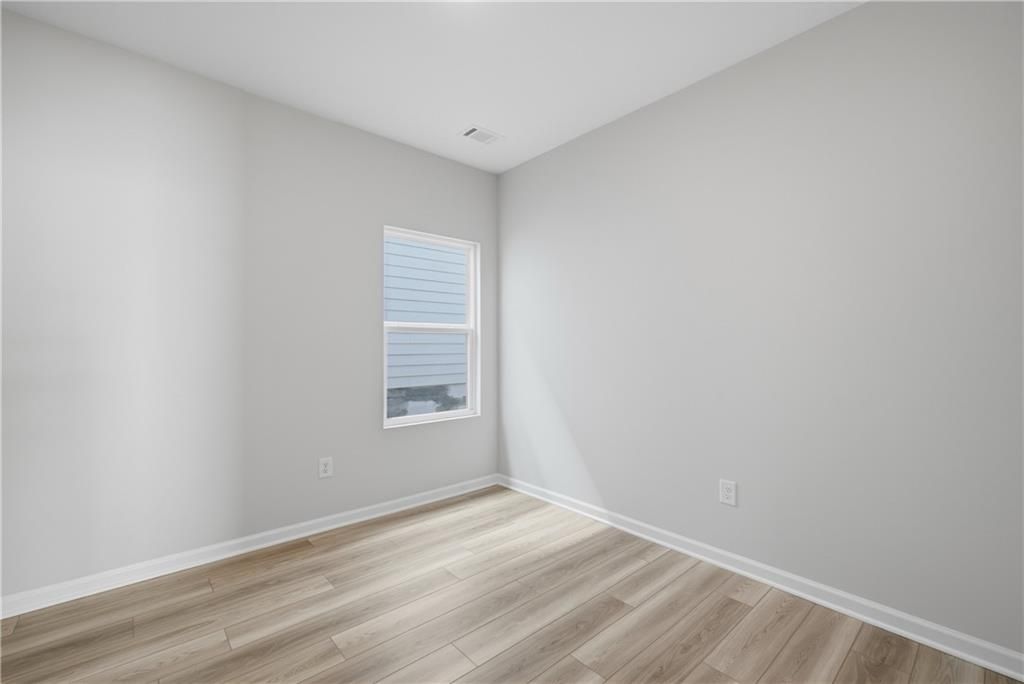 Bright empty bedroom with light wood-look flooring and window in Davidson Homes The Oconee B, The Bluffs, Canton, Georgia