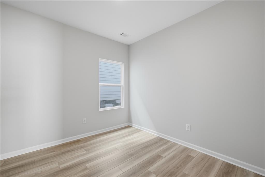 Bright empty bedroom with light wood-look flooring and window in Davidson Homes The Oconee B, The Bluffs, Canton, Georgia