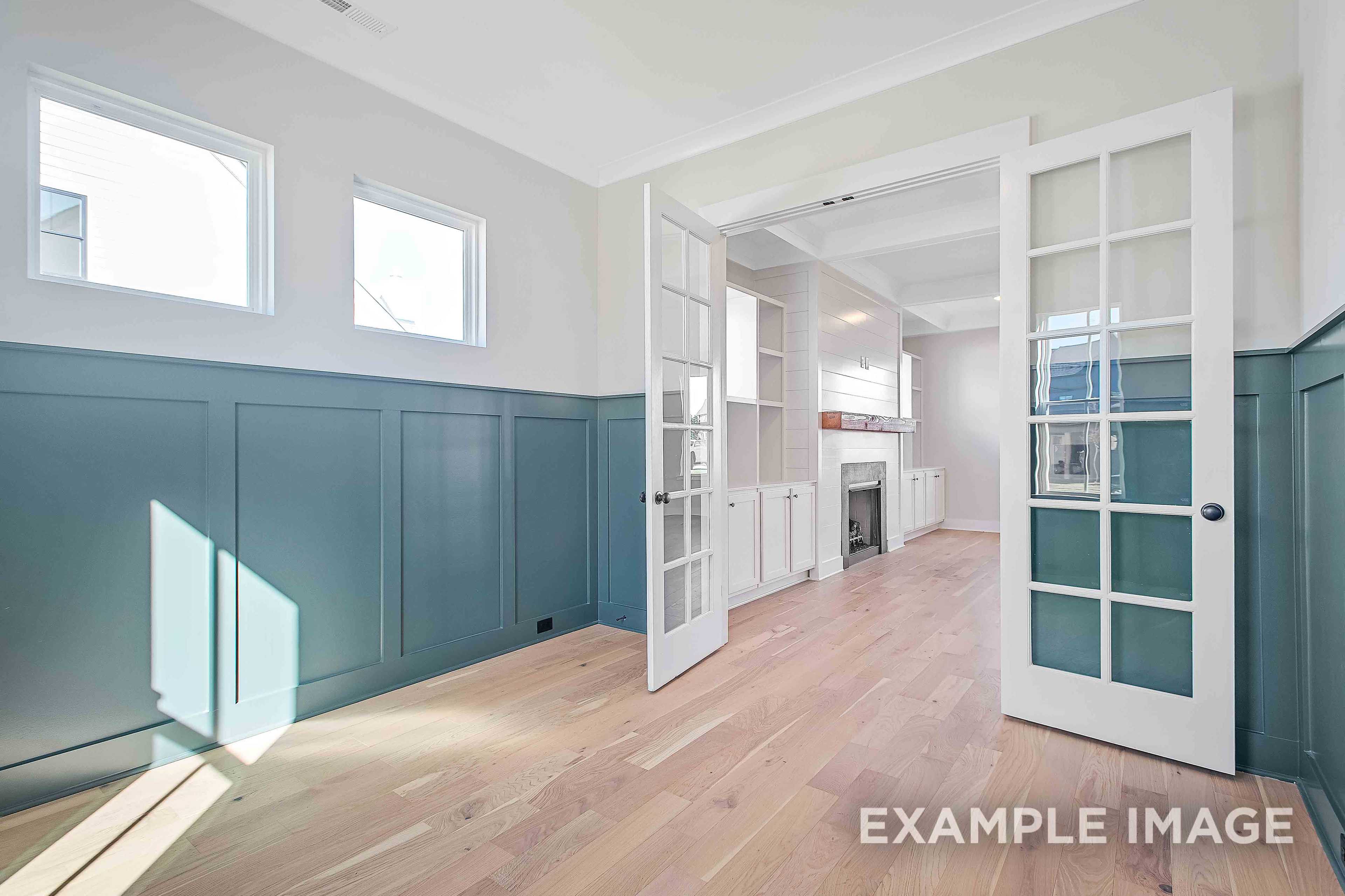Spacious living area in The Alston A with open French doors, cozy fireplace, teal wainscoting, hardwood floors, and natural light
