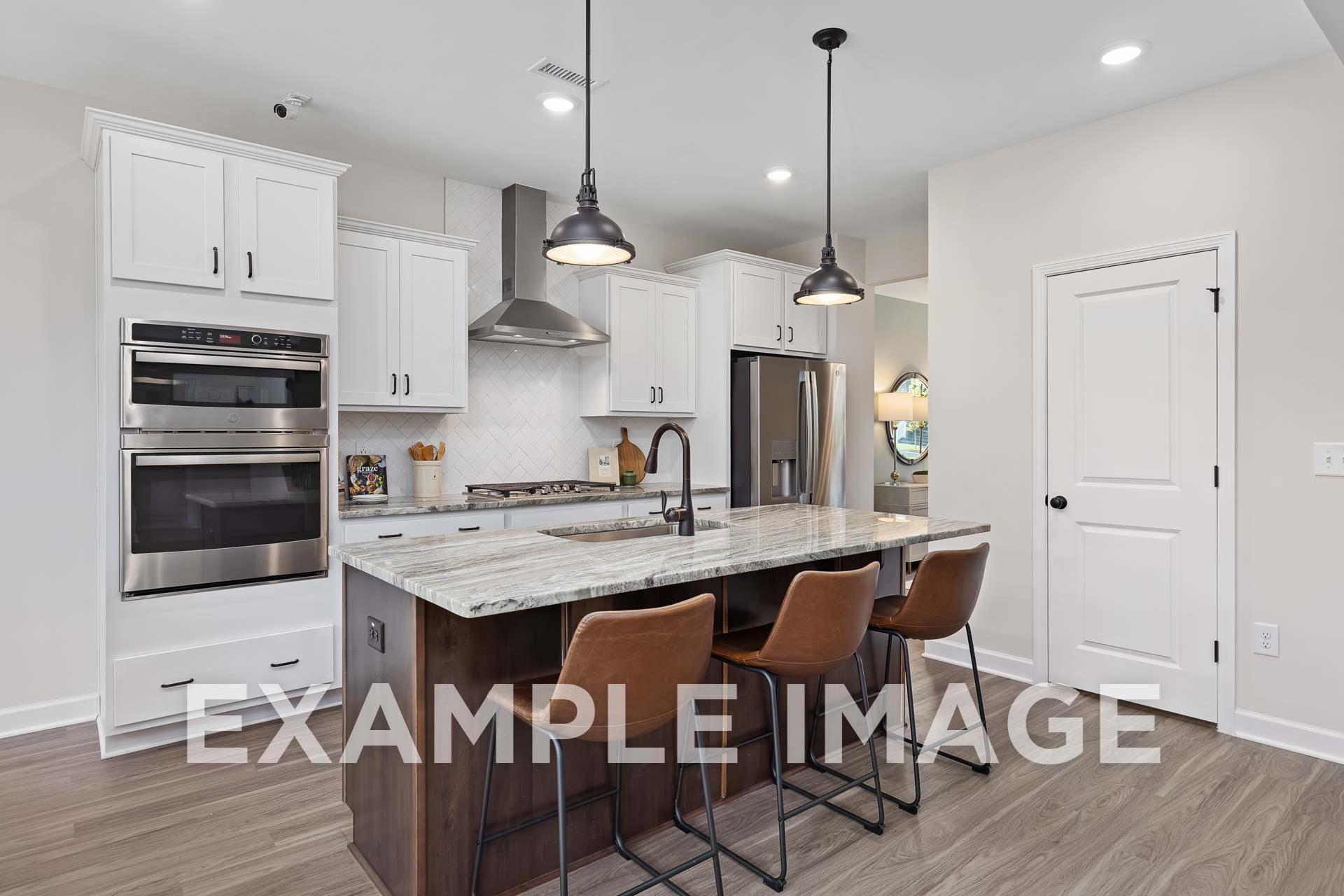 Modern kitchen in The Willow E showcasing white shaker cabinets, quartz island with bar stools, stainless steel appliances