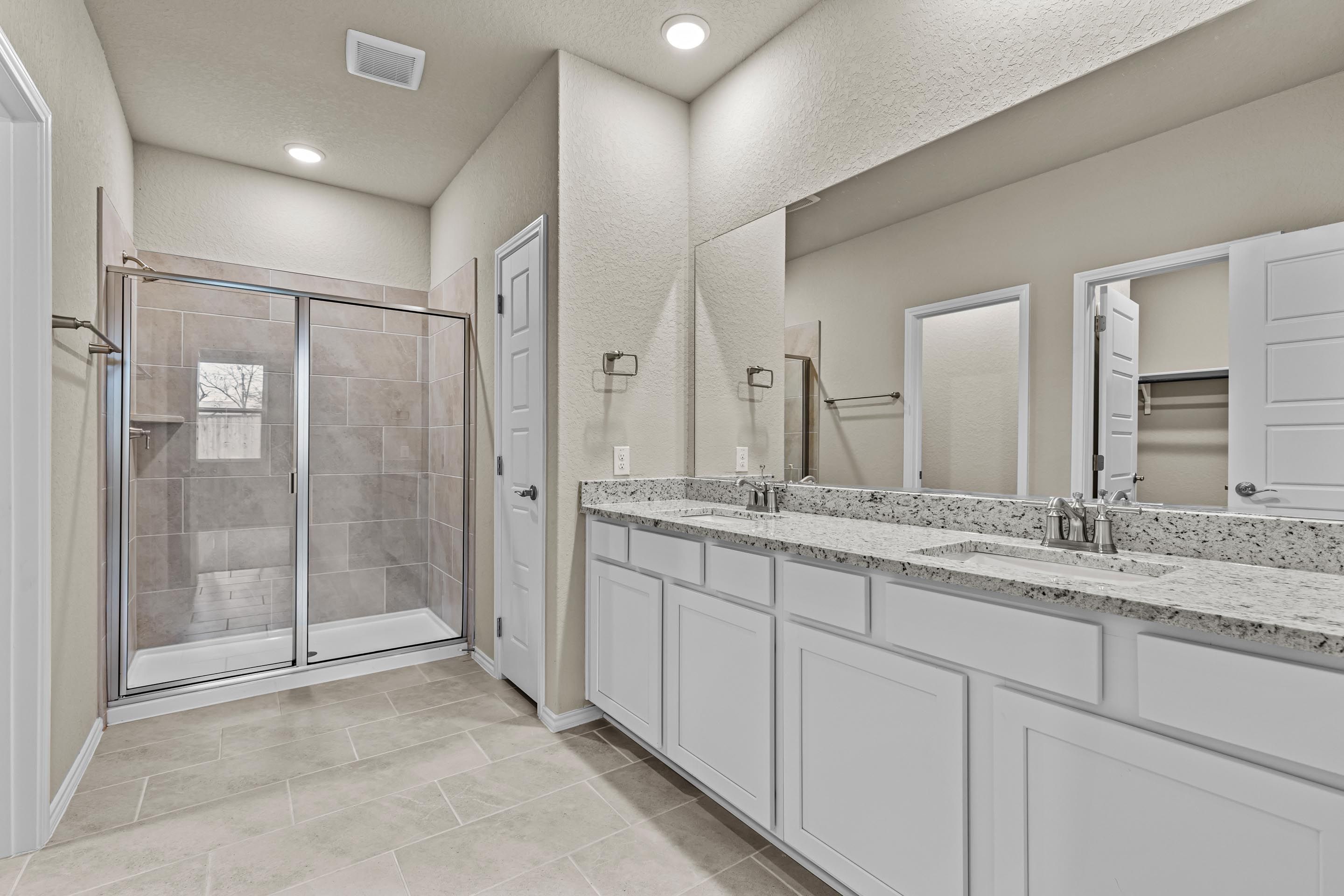 Modern master bathroom featuring dual vanities, quartz counters, and tiled walk-in shower in Davidson Homes The Douglas F, San Antonio