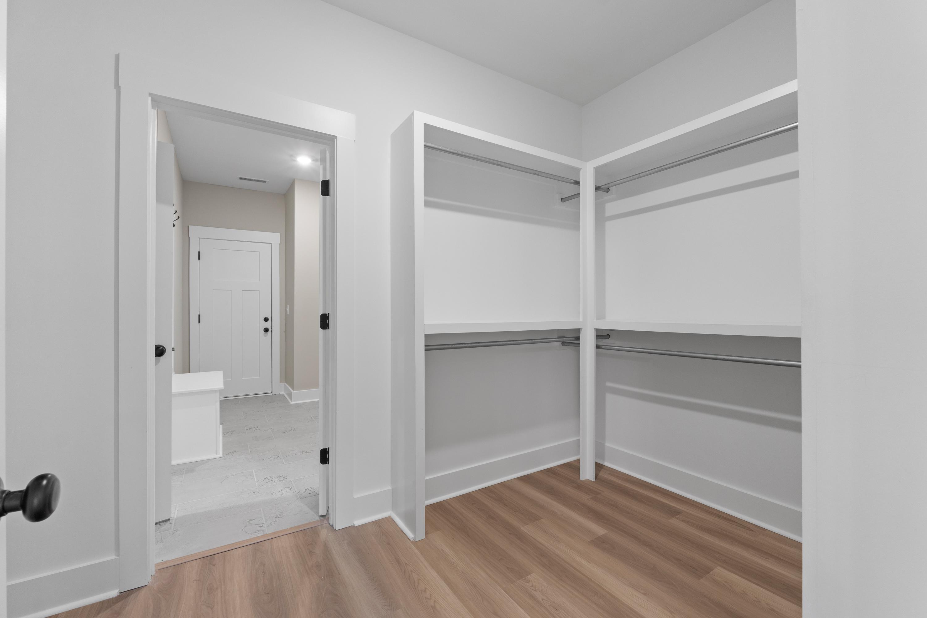 Spacious walk-in closet in The Oxford B master suite featuring white built-in shelves, hanging rods, and adjacent bathroom view