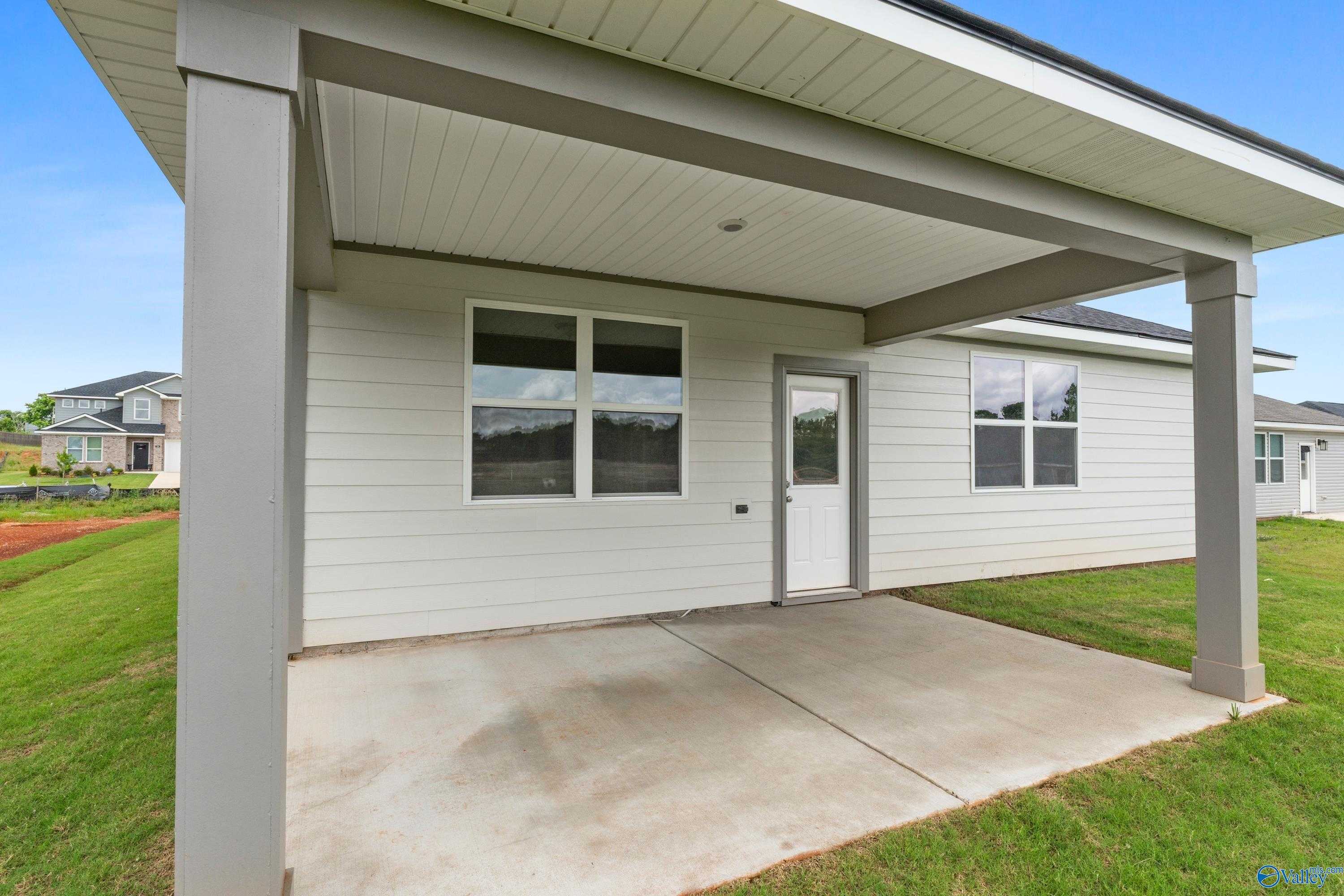 Covered back patio with concrete slab, white siding house, and yard view in Evermore Homes The Aurora, Carroll Green, Harvest, Alabama