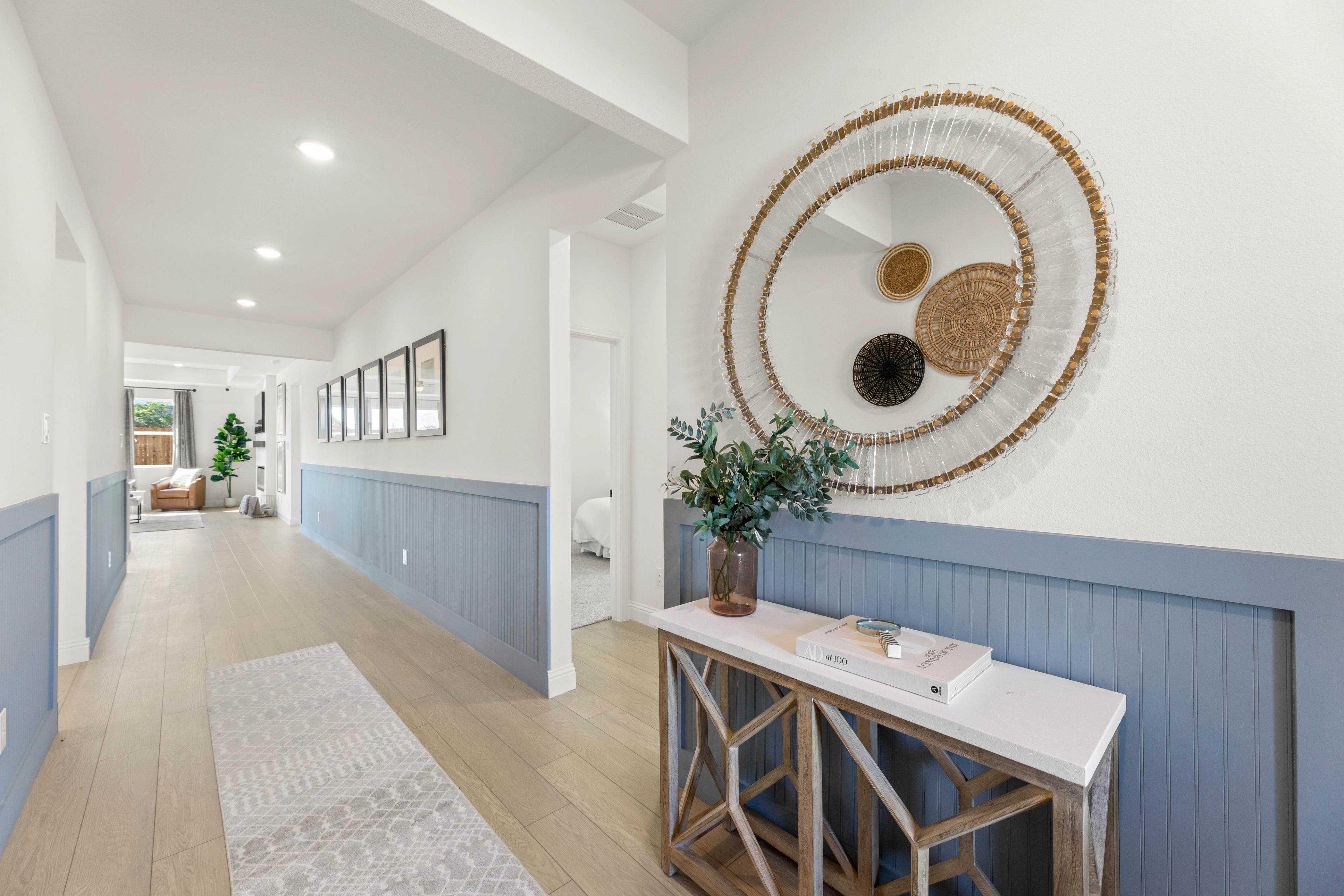Spacious entry hallway in The Laurel G with blue wainscoting, round woven mirror, console table, and greenery