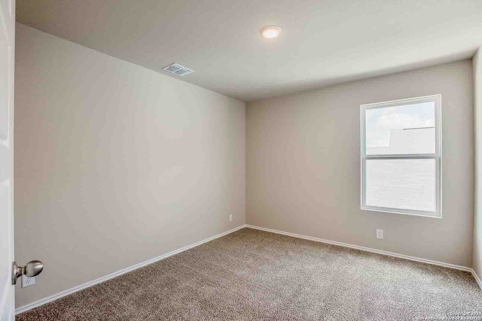 Spacious empty bedroom with beige walls, plush carpet floor, large sunny window in Davidson Homes The Murray H, Seguin, Texas