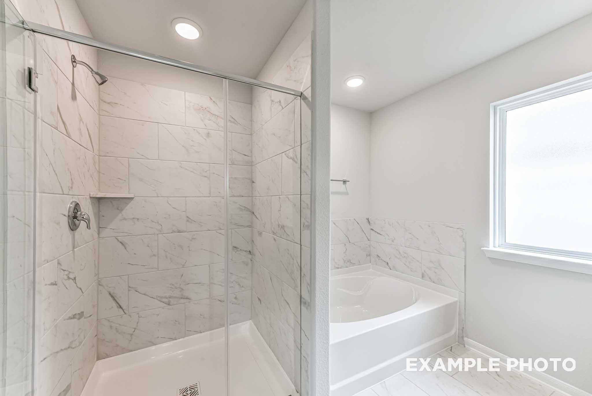 Marble-tiled walk-in shower and garden tub in primary bathroom of Davidson Homes The Costa A plan in Dayton, Texas
