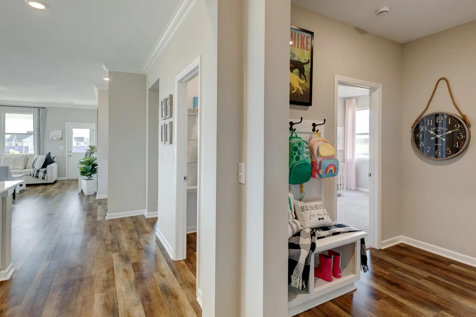 Open-concept kitchen and entry hallway in The Aurora A, featuring white island cabinets, hardwood floors, wall hooks with backpacks, and shoe storage