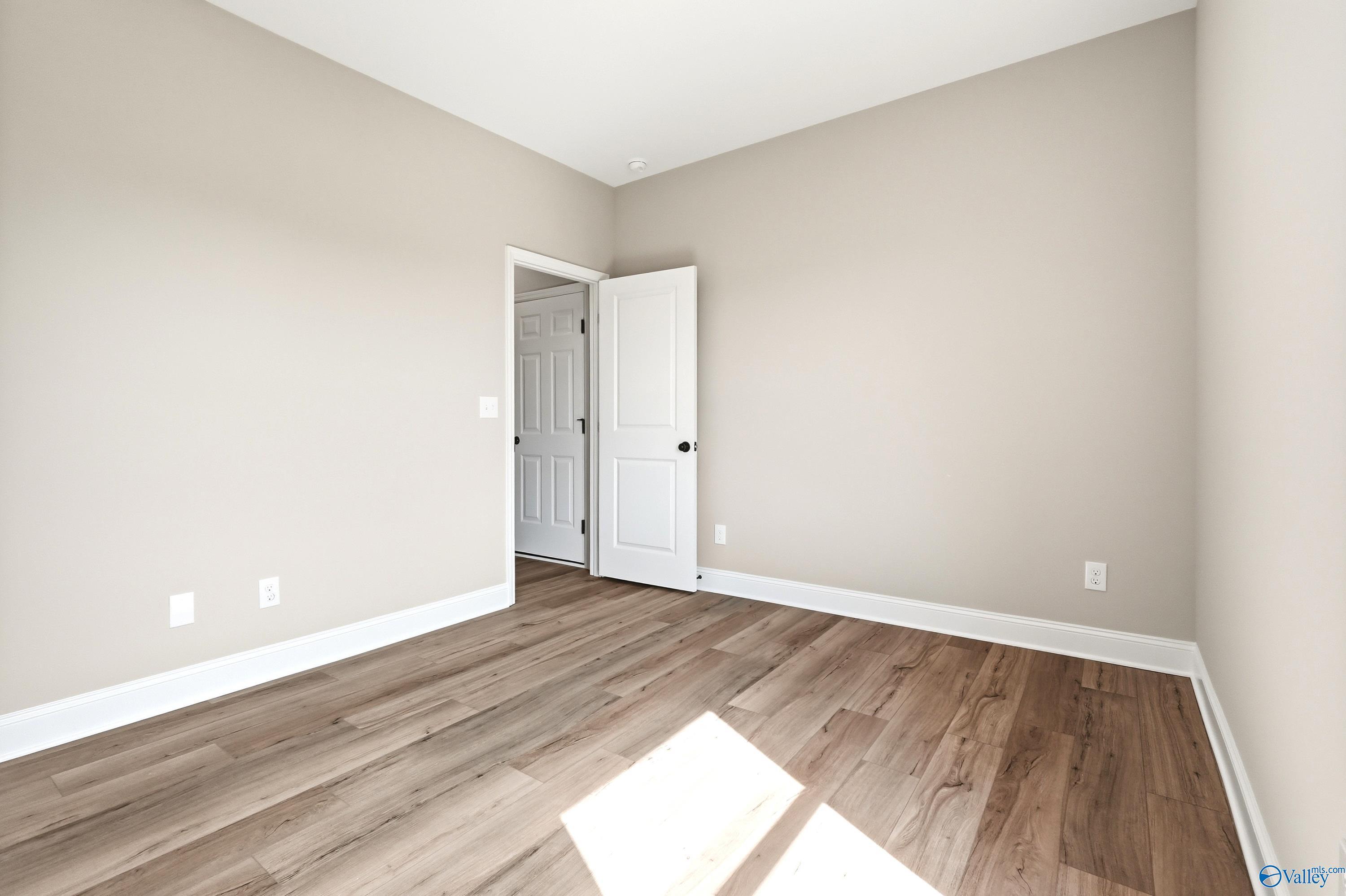 Spacious secondary bedroom with wood-look flooring in The Daphne D floor plan at Creekside in Harvest, Alabama.