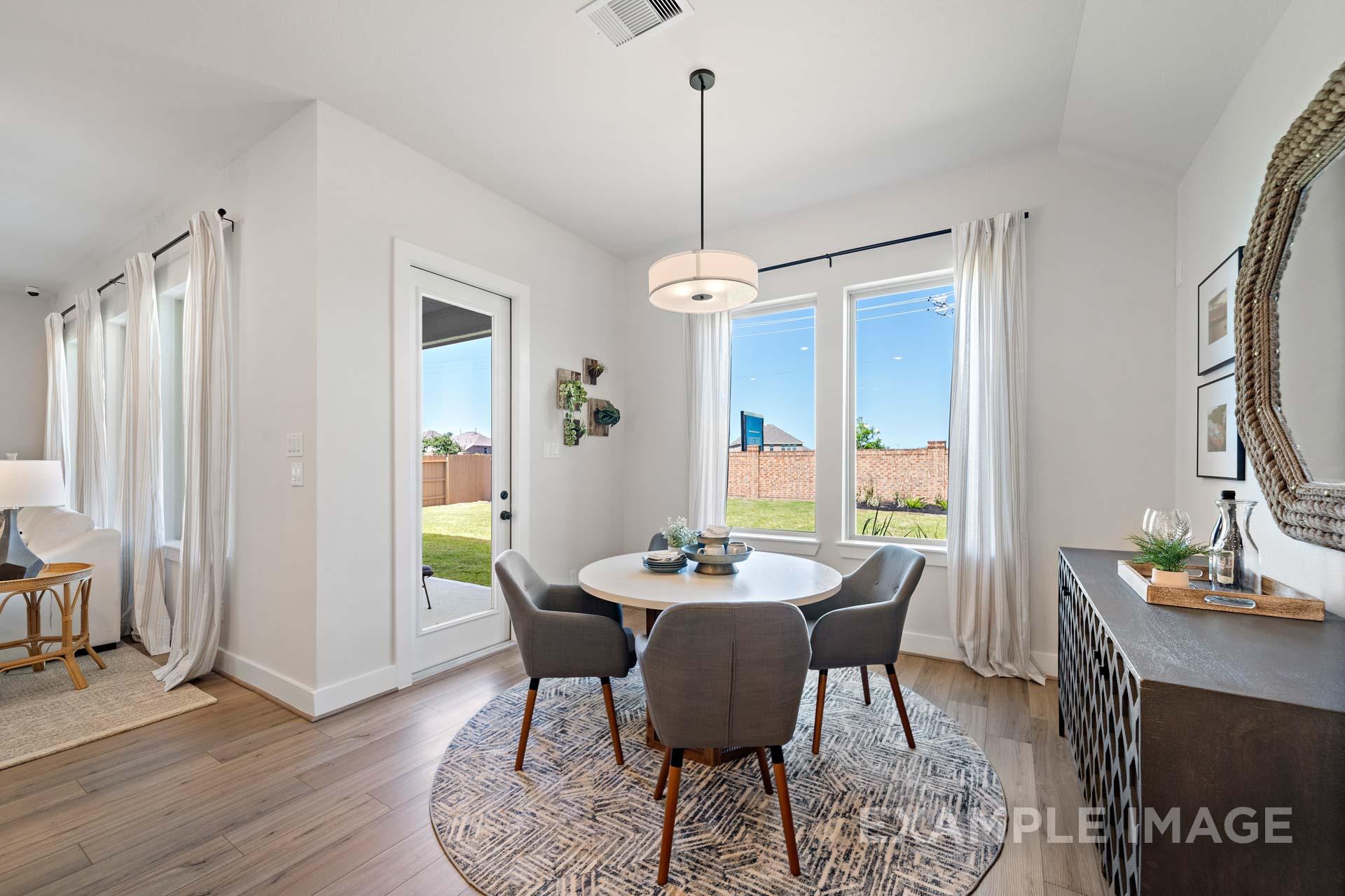 Bright dining room in The Edward C home by Davidson Homes with round table, gray chairs, chandelier, and sliding doors to backyard view