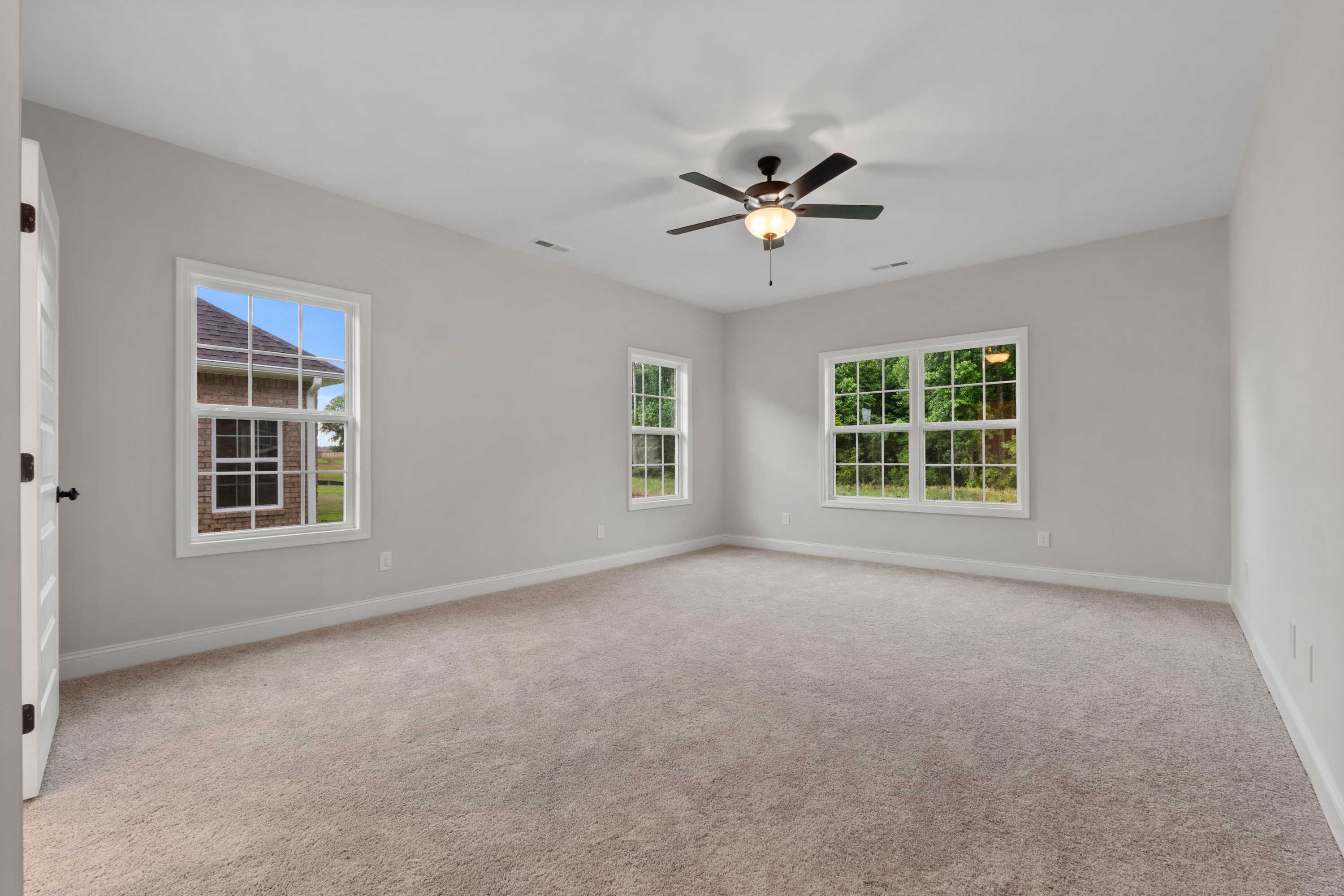 Spacious bedroom in The Oxford Davidson Homes design featuring light gray walls, beige carpet, large windows, and ceiling fan