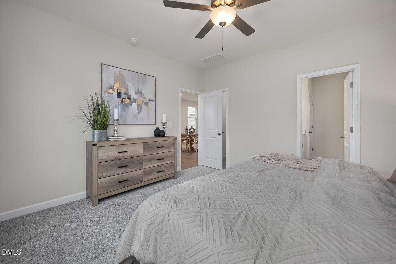 Cozy master bedroom with beige walls, ceiling fan, wooden dresser, abstract art, and king bed in Davidson Homes The Carter C, Lillington, NC