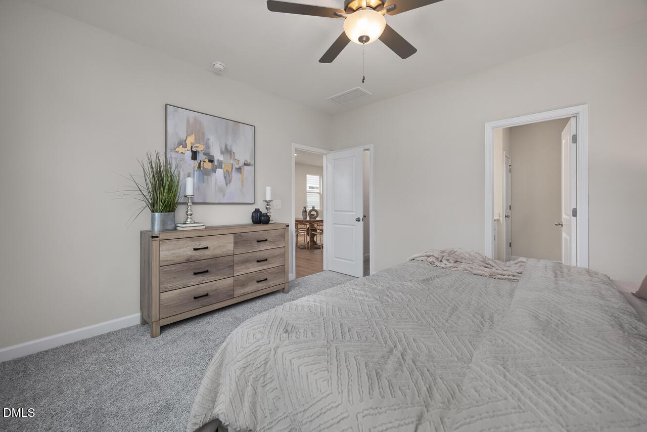 Serene master bedroom with plush gray bed, wooden dresser, ceiling fan, and en-suite bath in Davidson Homes The Carter C, Lillington, NC