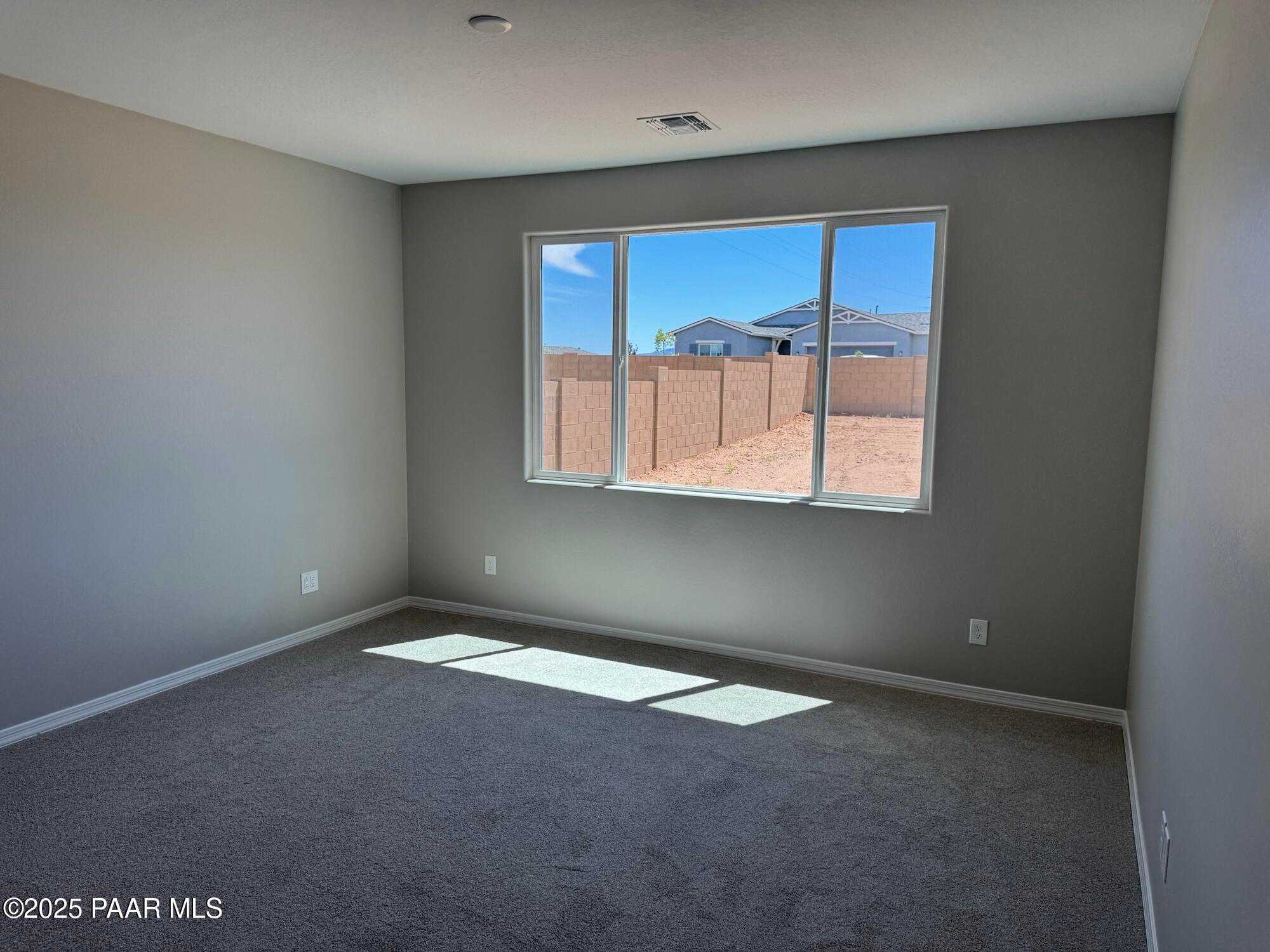 Bright empty bedroom with gray carpet, light walls, and large window view of sunny backyard in The Sheridan II B, Prescott, AZ