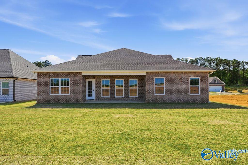 Rear view of The Harrison brick home with covered patio, large grassy yard, and 2-car garage in Cain Park, Hartselle, Alabama