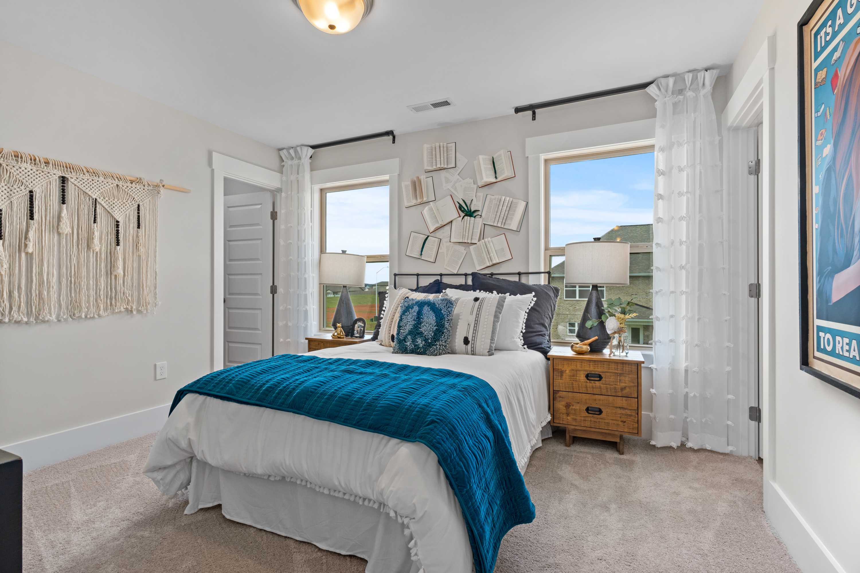 Spacious master bedroom in The Chelsea B with blue bedding, macrame wall art, and large windows in Davidson Homes design