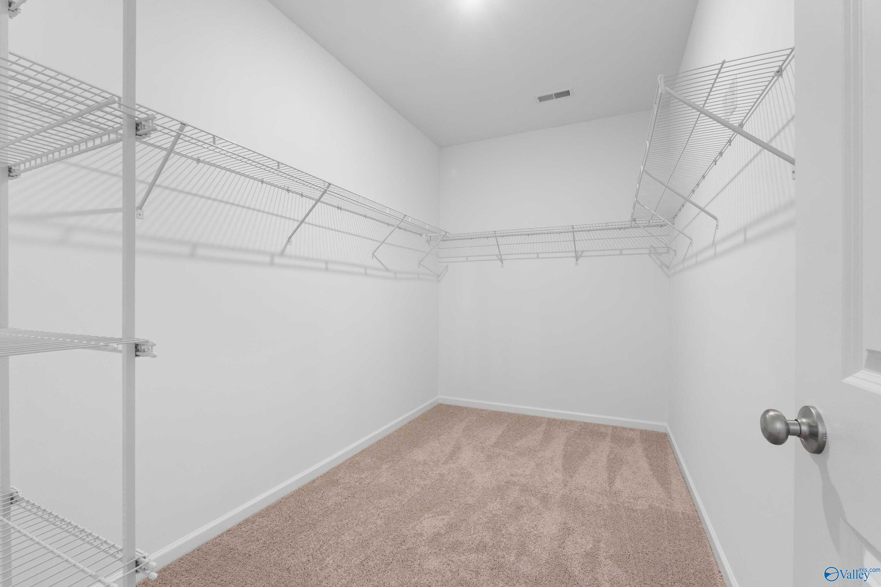 Spacious walk-in closet with white wire shelving, beige carpet in Davidson Homes The Orion, Athens, Alabama