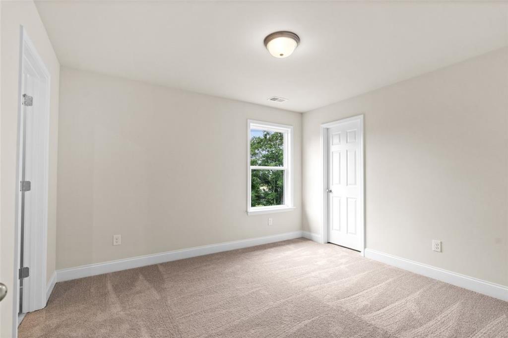 Cozy bedroom with beige walls, plush carpet, double closet doors, and tree-view window in Davidson Homes The Hickory B at Wehunt Meadows, Hoschton